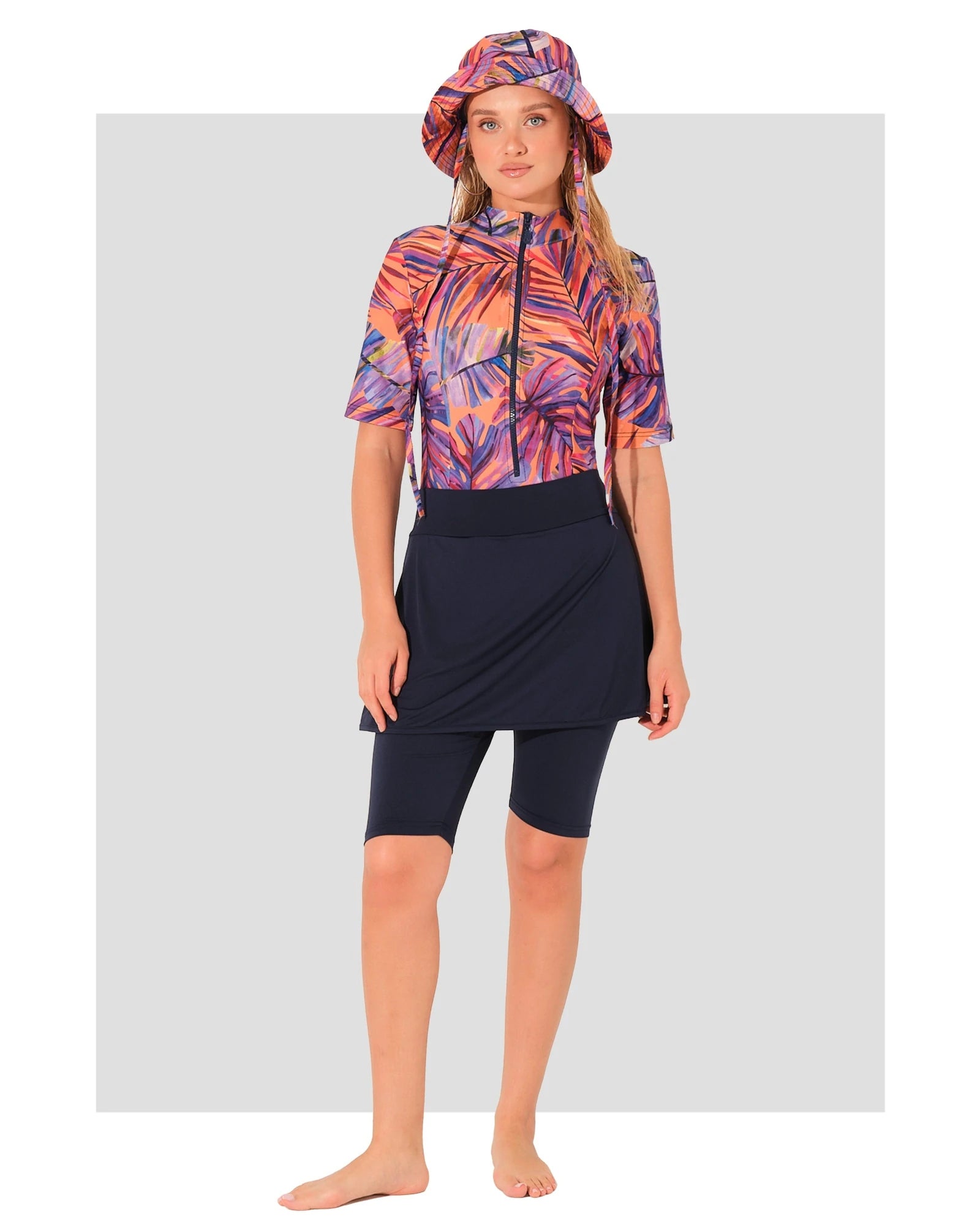 Woman in tropical print burkini set with dark swim skirt and hat.