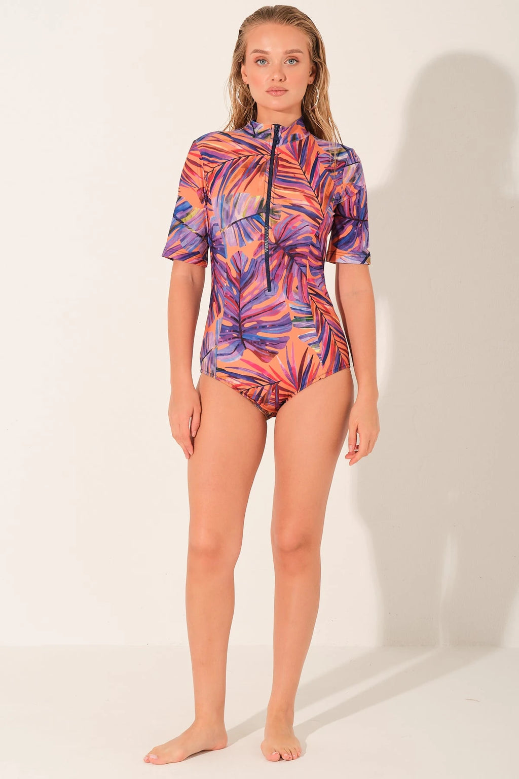 Woman wearing a tropical print short-sleeve swim top with front zipper.