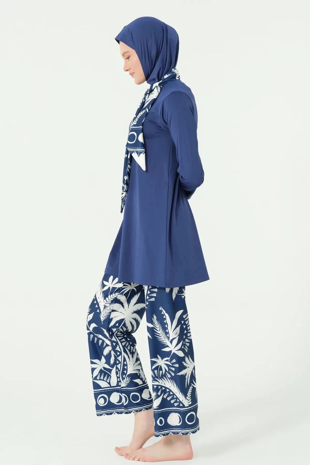 Woman in navy Lycra burkini with white palm print pants, side profile.
