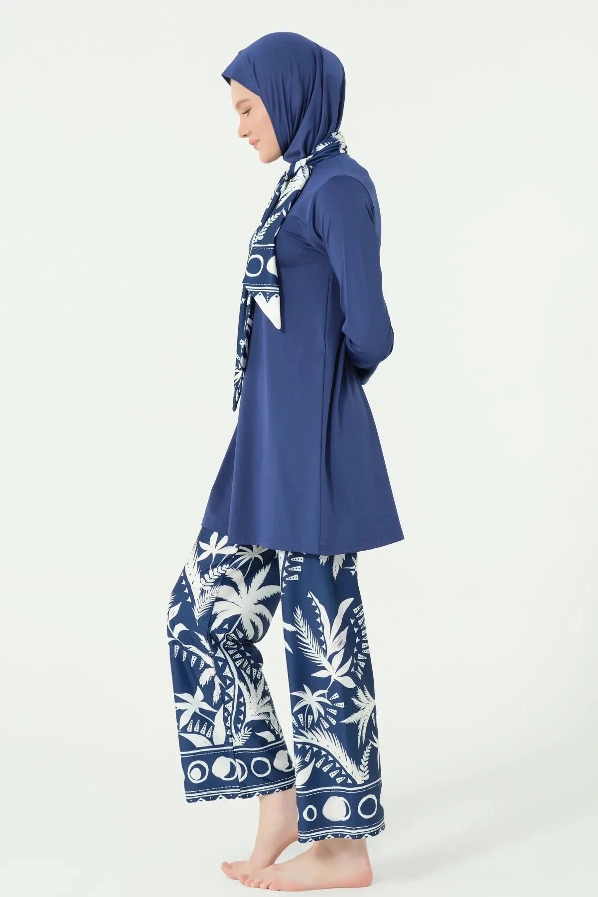 Woman in navy Lycra burkini with white palm print pants, side profile.