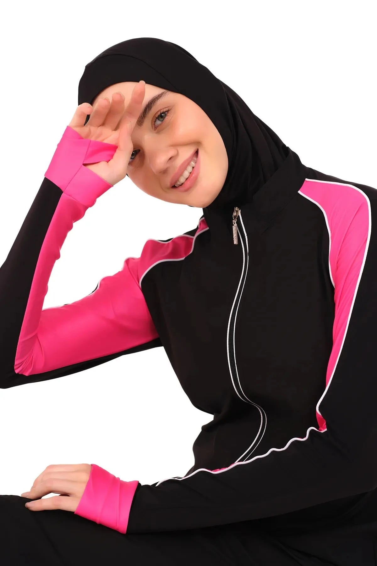 Smiling model wearing black burkini with pink sleeves, hand shielding eyes.