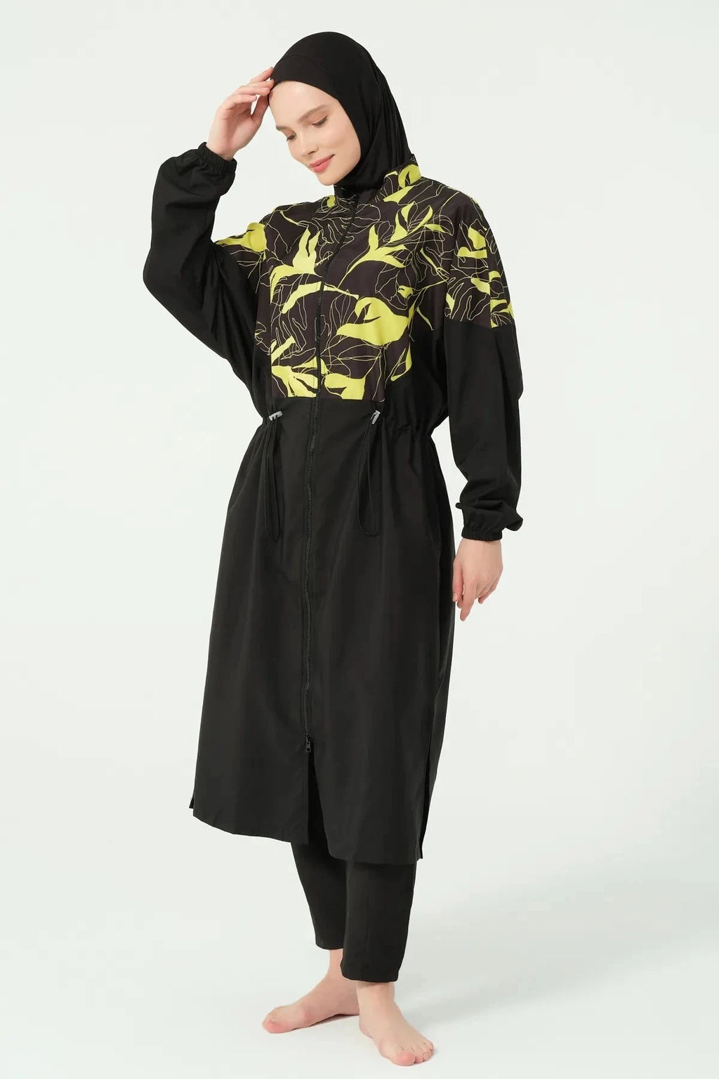 Woman in a black and yellow tropical print burkini set, standing.