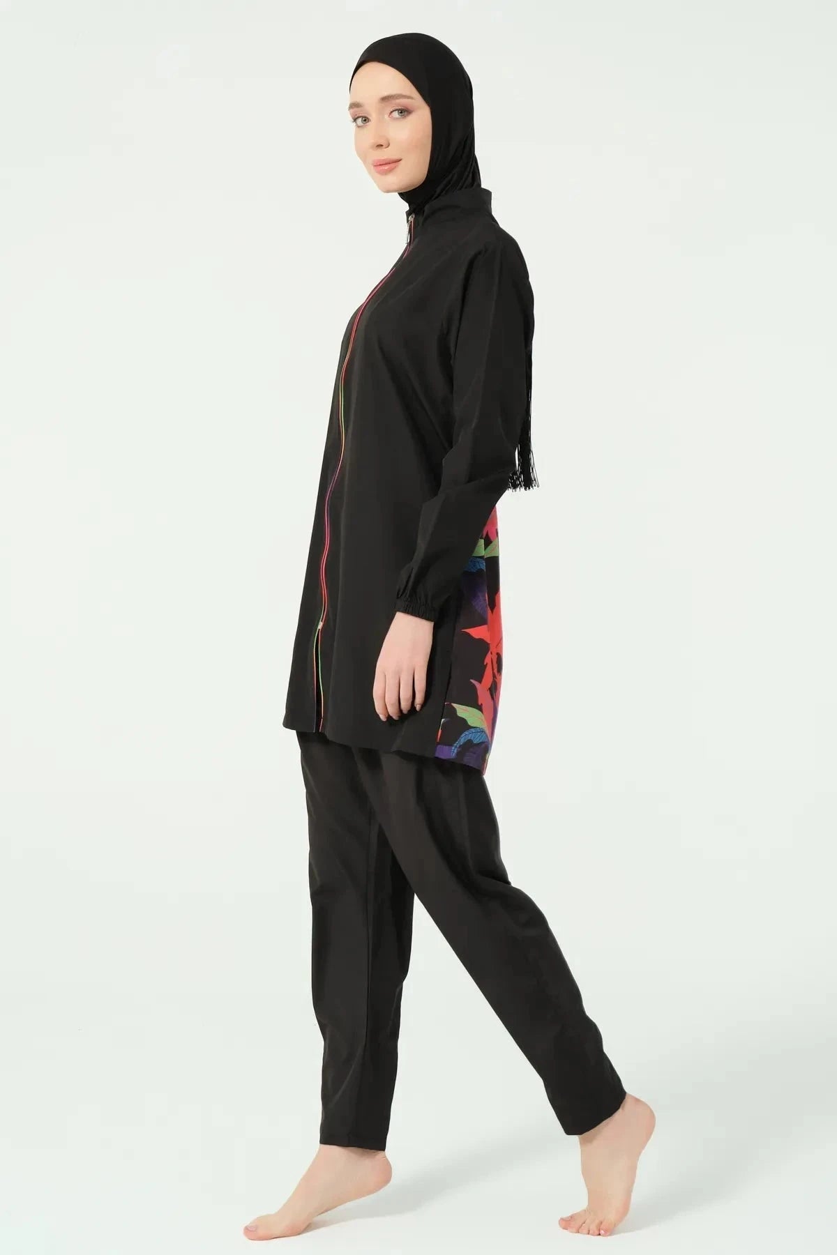 Model in black burkini with tropical print, side view on white background.