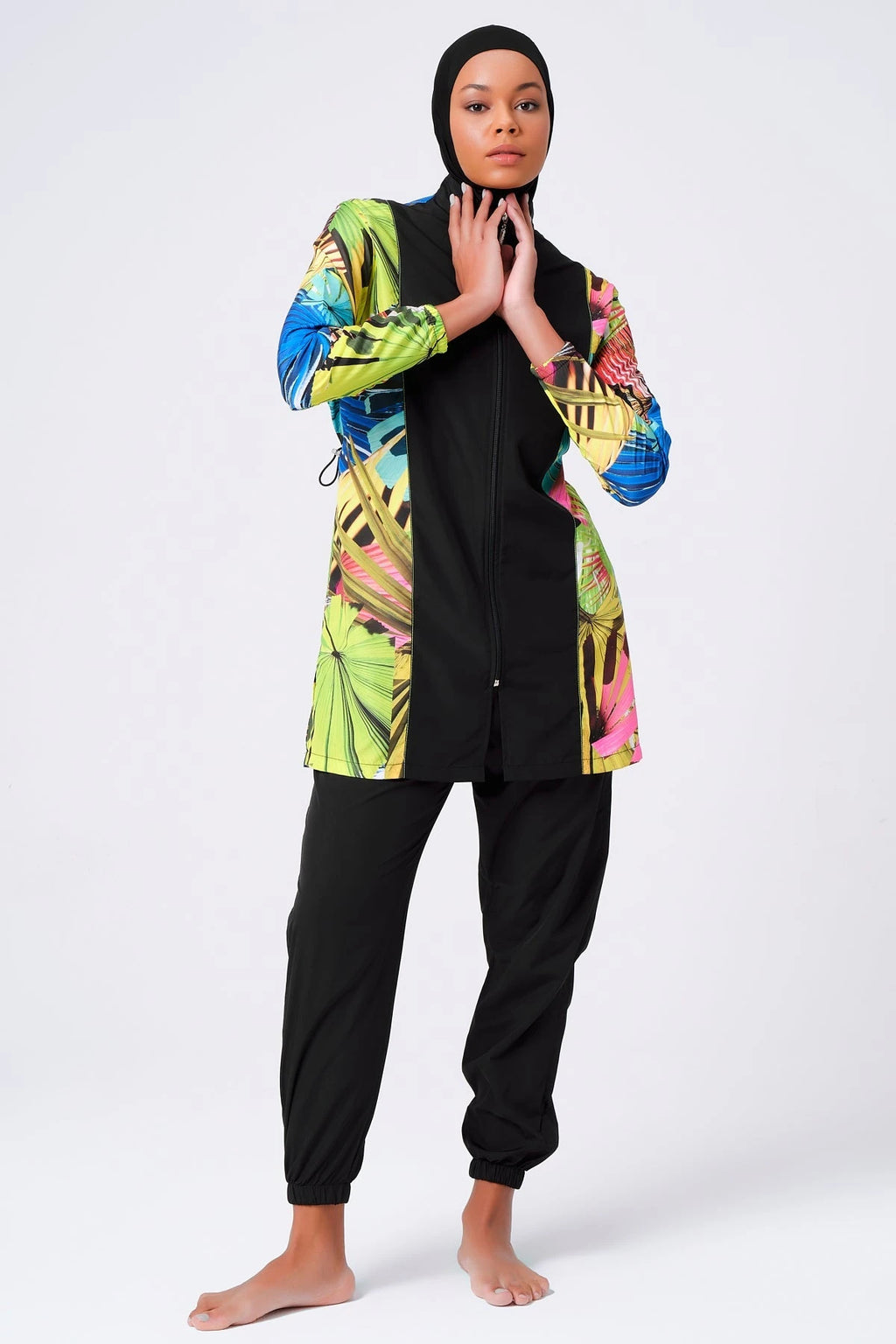 Woman in tropical print burkini, black hijab, hands near neck.