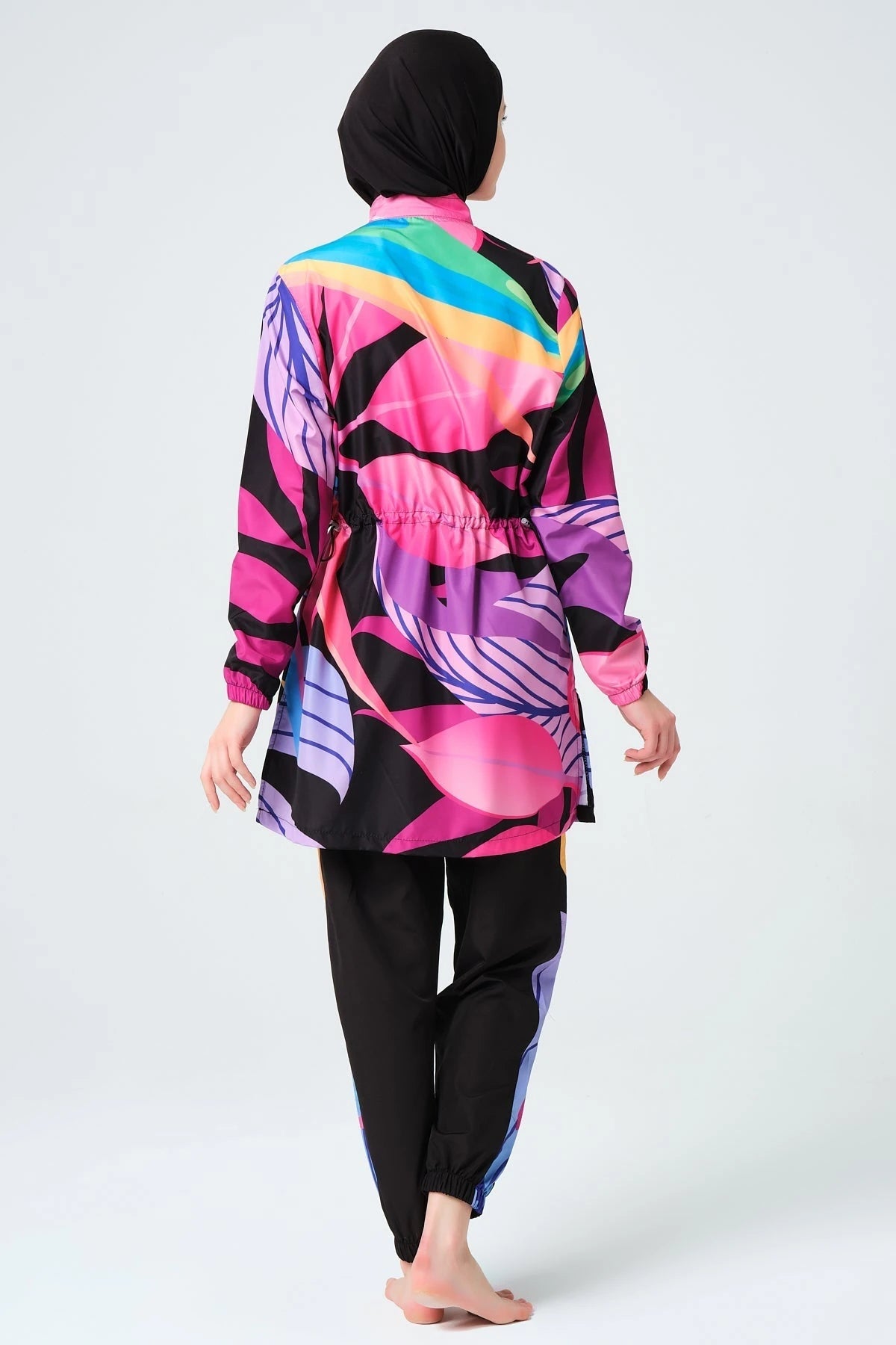 Model wearing vibrant tropical print burkini with cinched waist, back view.