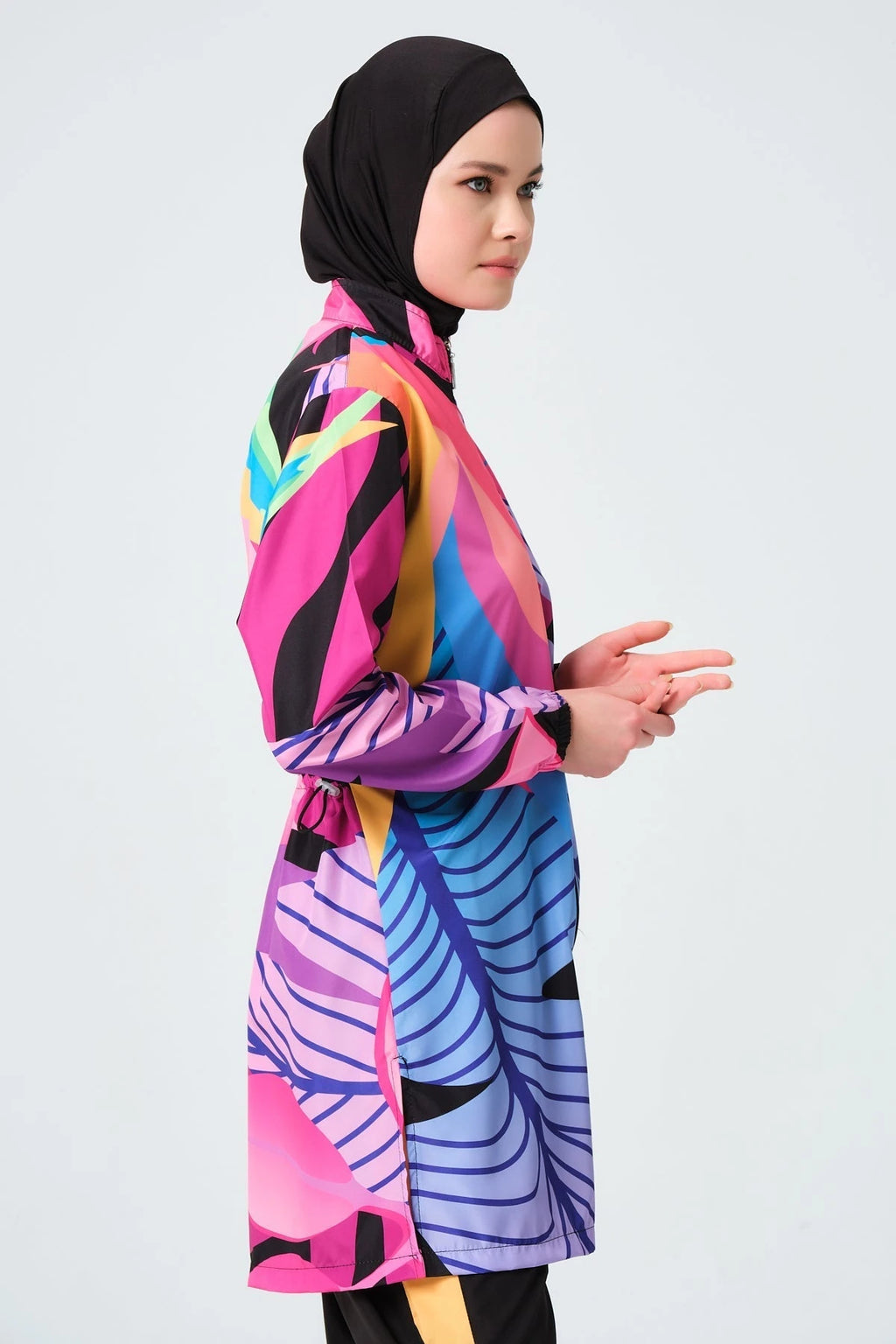 Model in vibrant tropical print burkini, side pose, hands clasped.