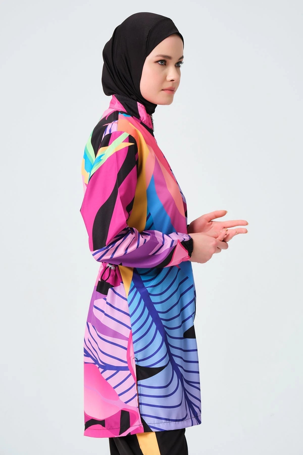 Model in vibrant tropical print burkini, side pose, hands clasped.