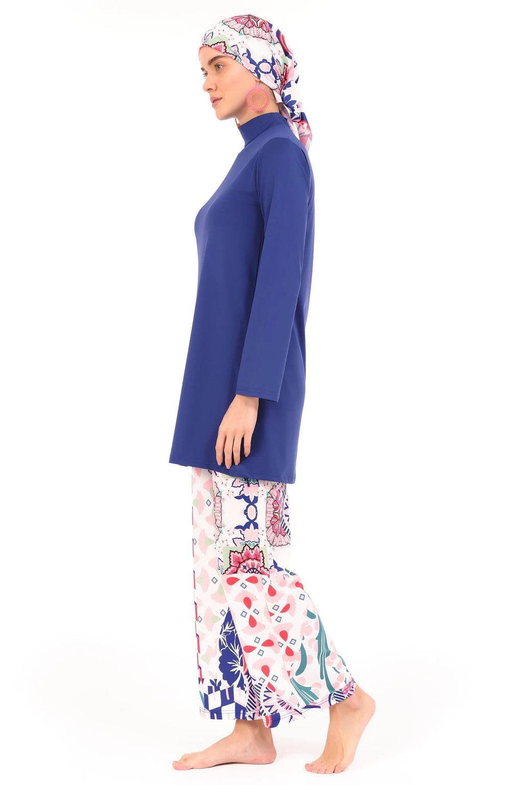 Model in blue and patterned burkini set, side view, walking on white background.