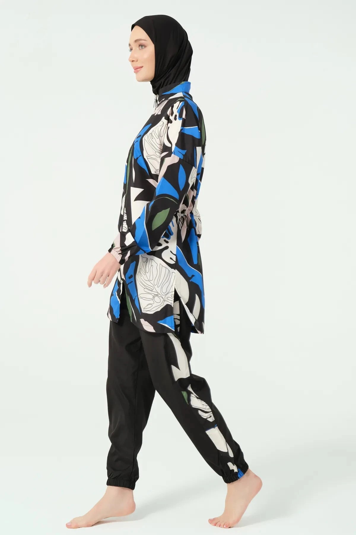 Woman in abstract print burkini set and black hijab, walking side view.