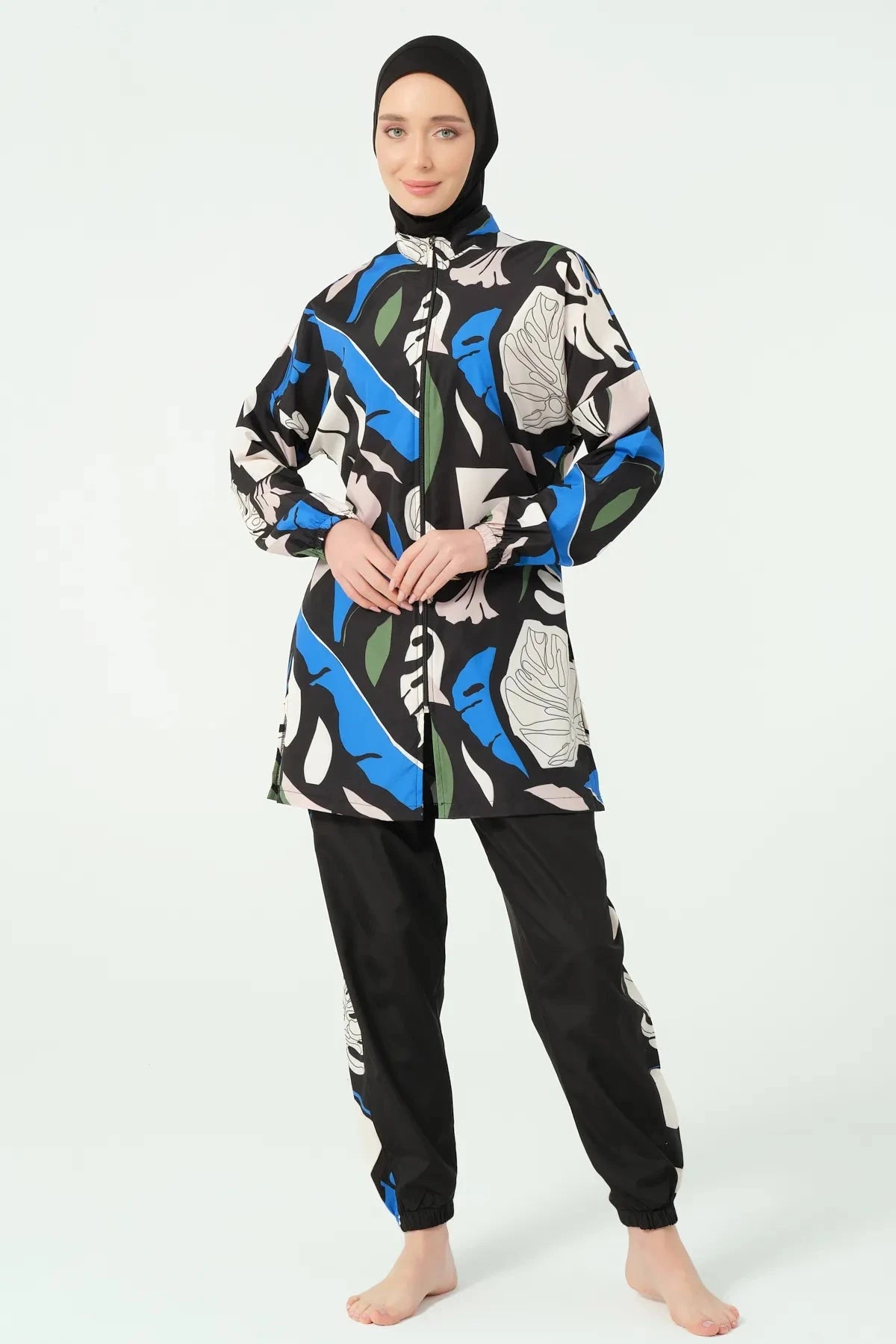 Woman wearing abstract print burkini set with black hijab, full body pose.