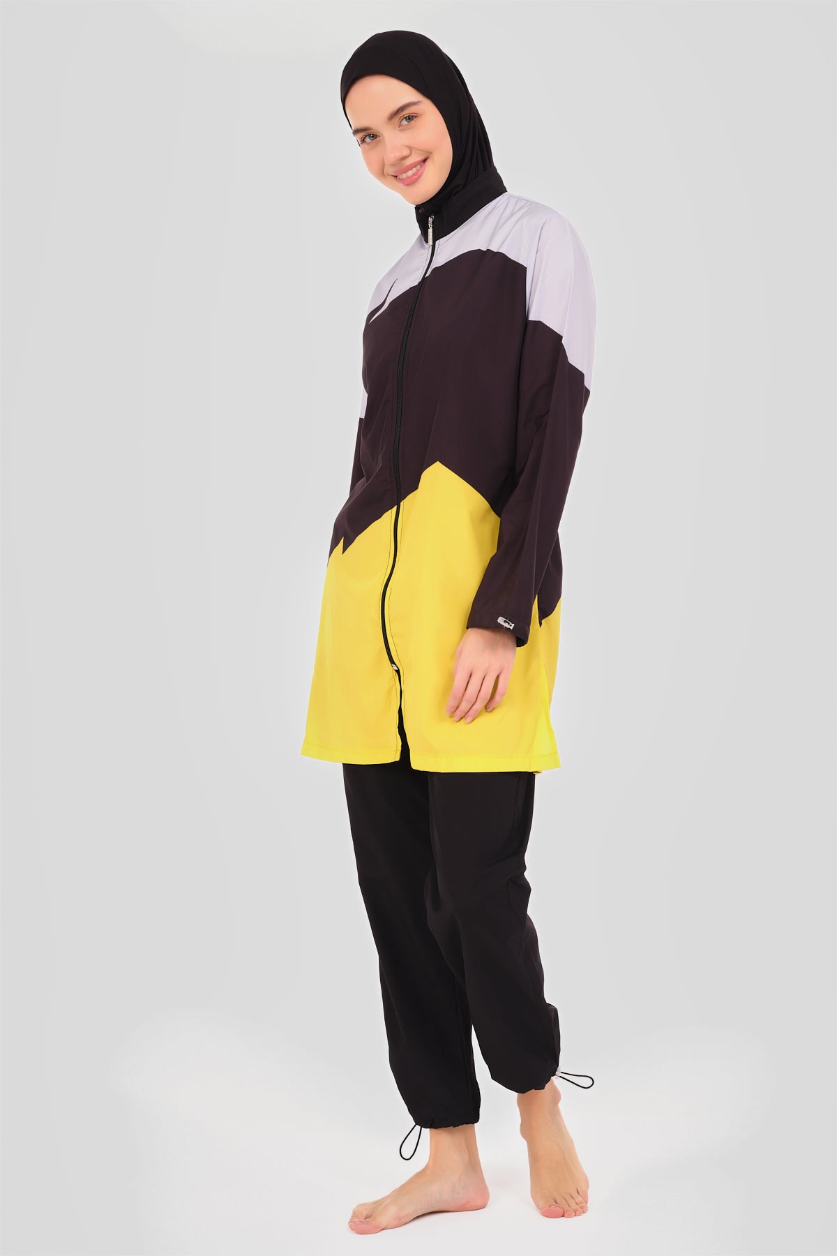 Model wearing sporty color-block burkini, black, yellow, and light grey, side pose.
