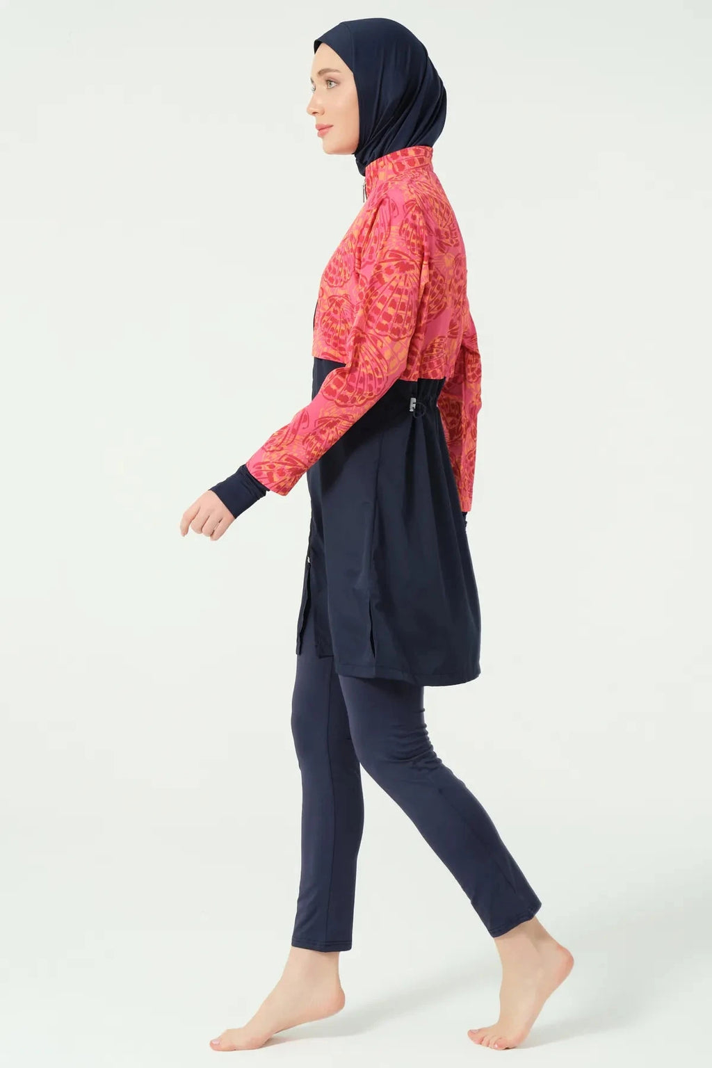 Woman in navy and coral burkini walking in side profile.