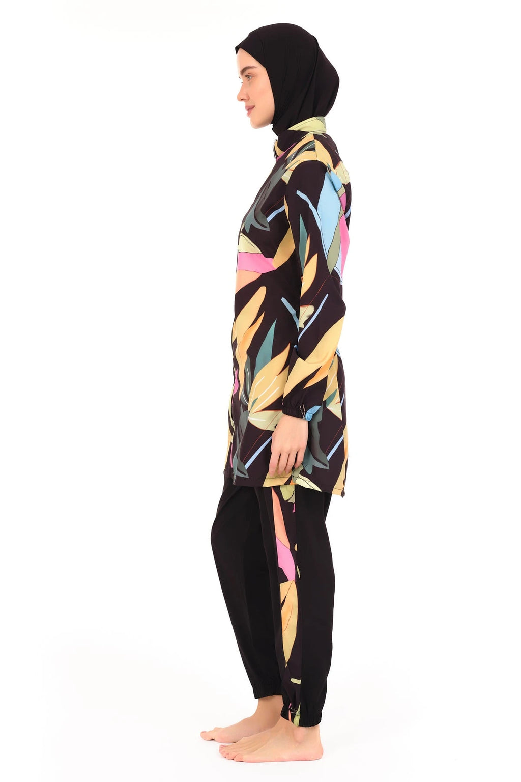 Side view of woman wearing black tropical print burkini and swim cap.