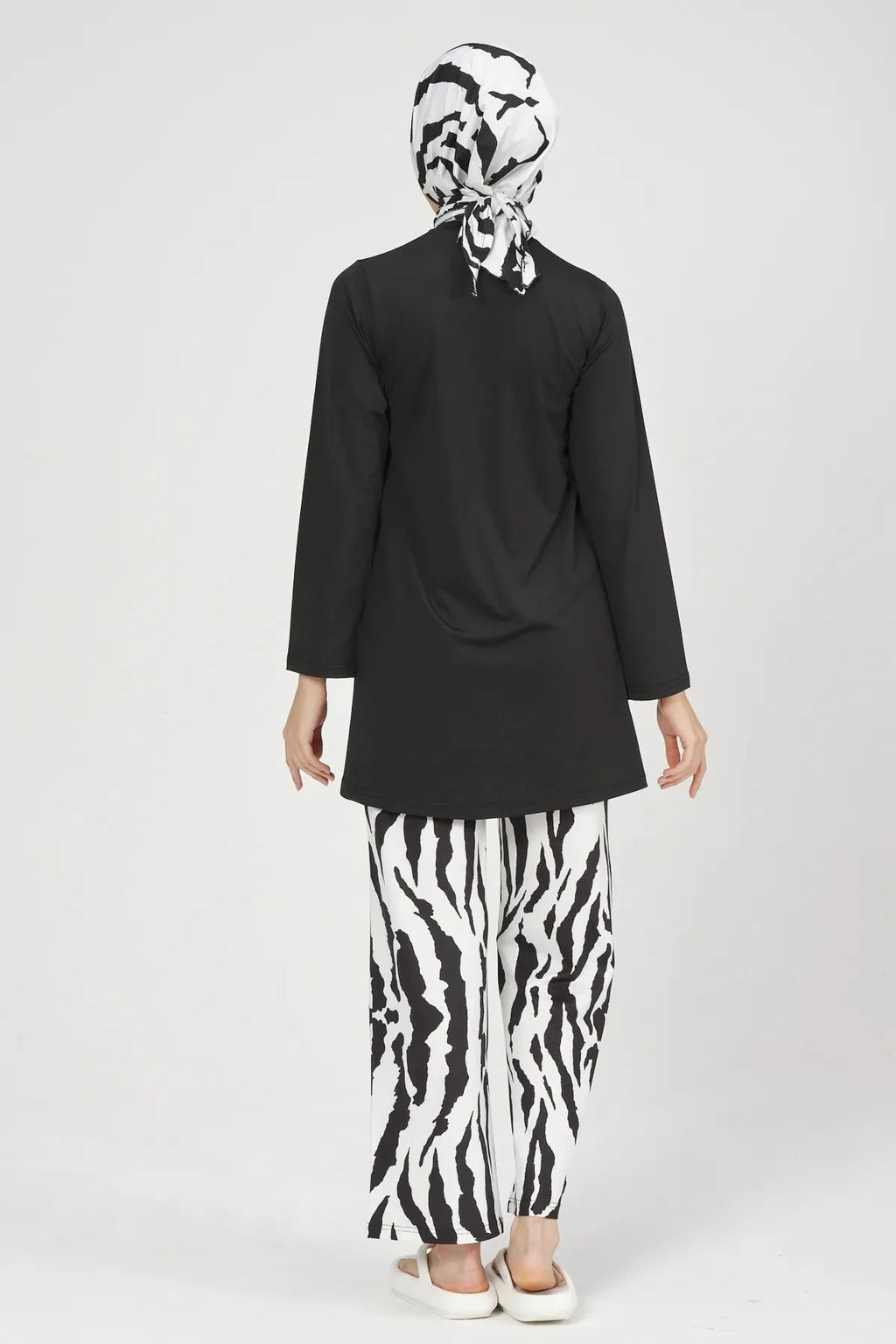 Woman in black tunic and zebra print burkini pants from behind.