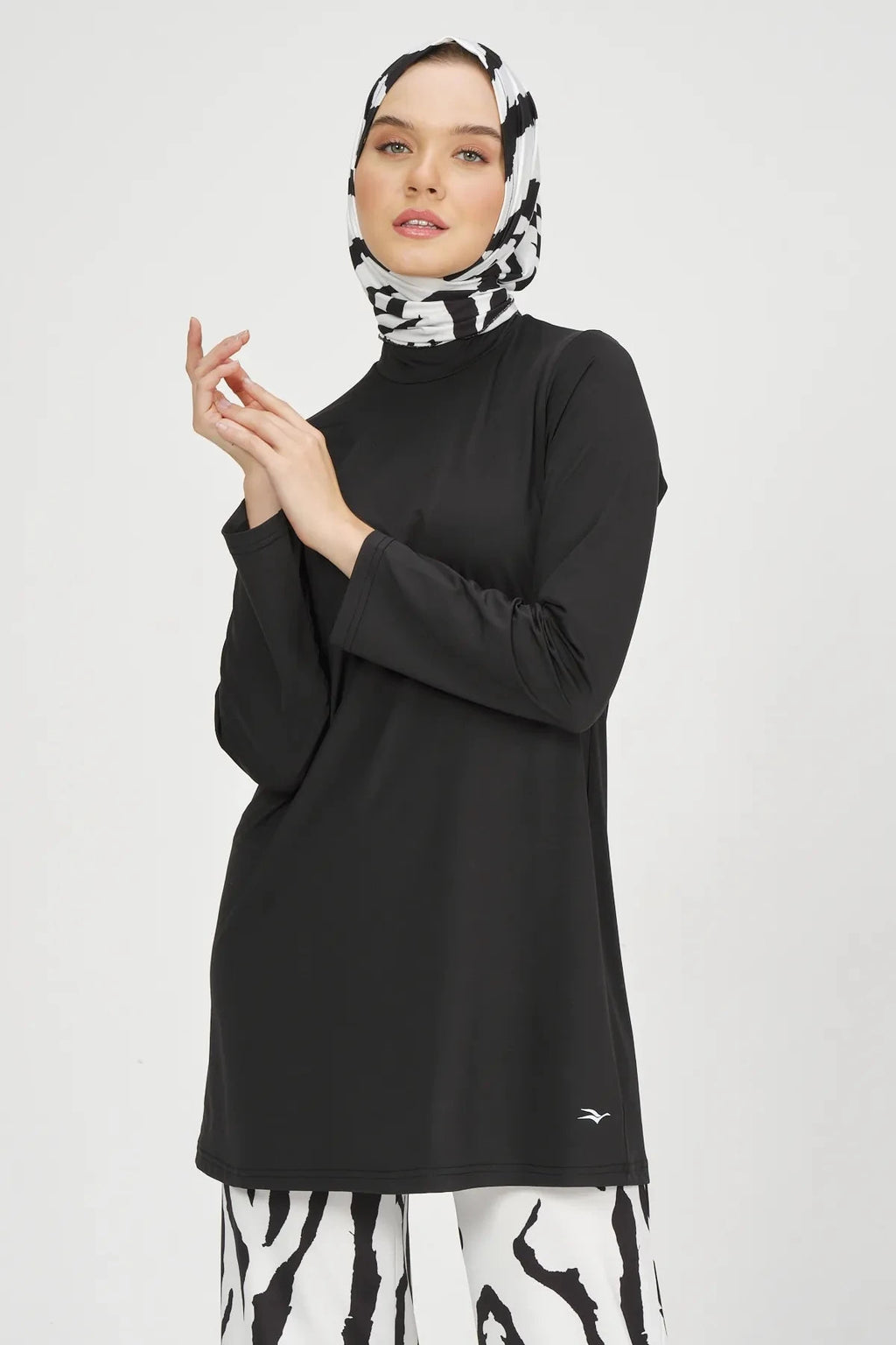 Woman in black burkini tunic and zebra print hijab, hands clasped.