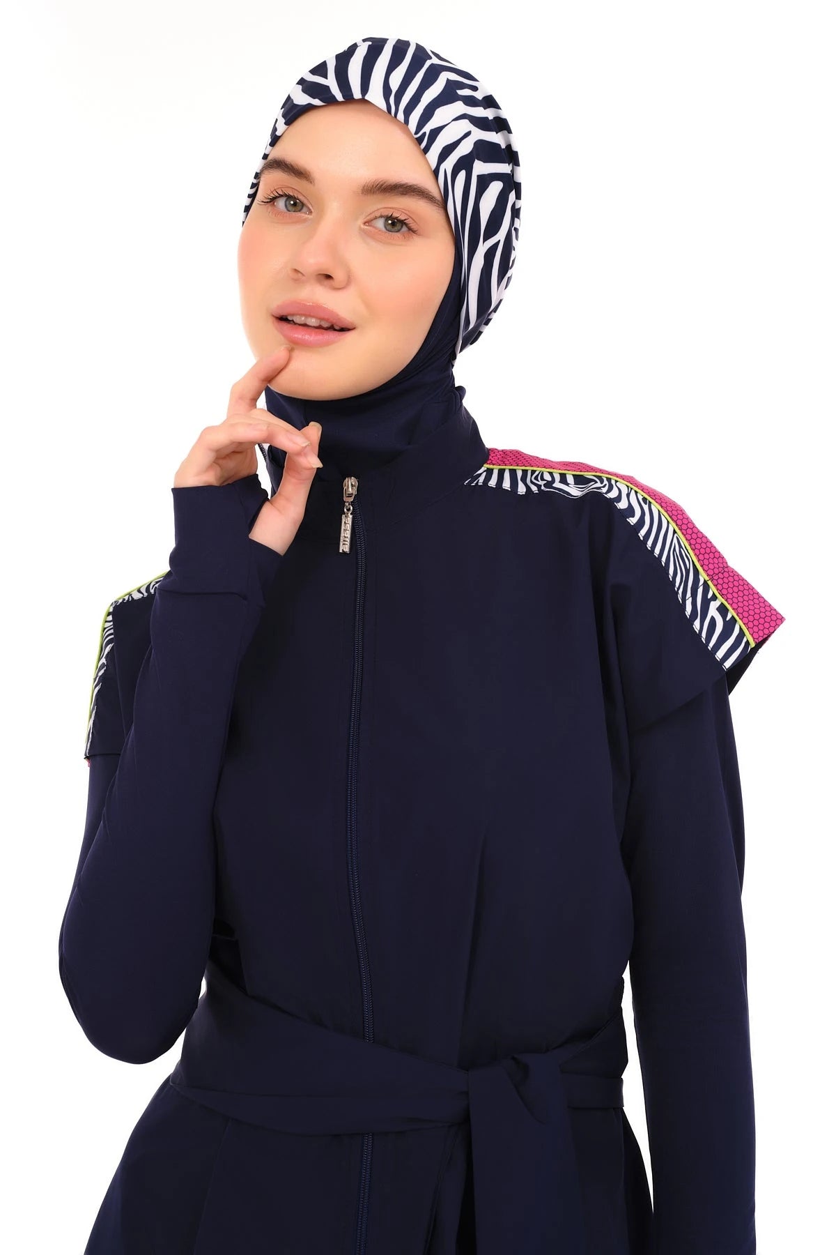 Model in navy burkini set with zebra print hijab, hand near chin.