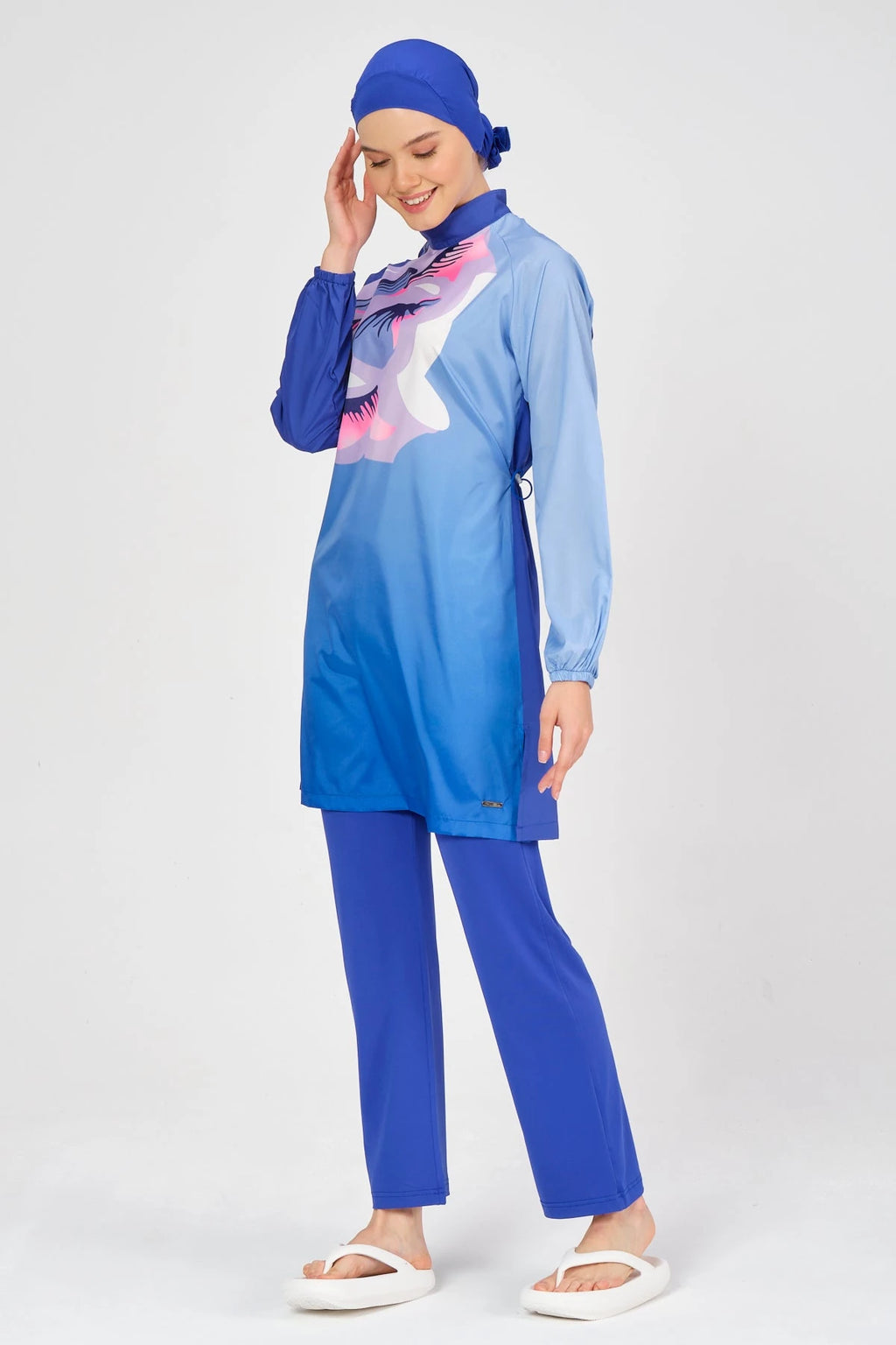 Model smiling in blue modest swimsuit with abstract print, front pose.