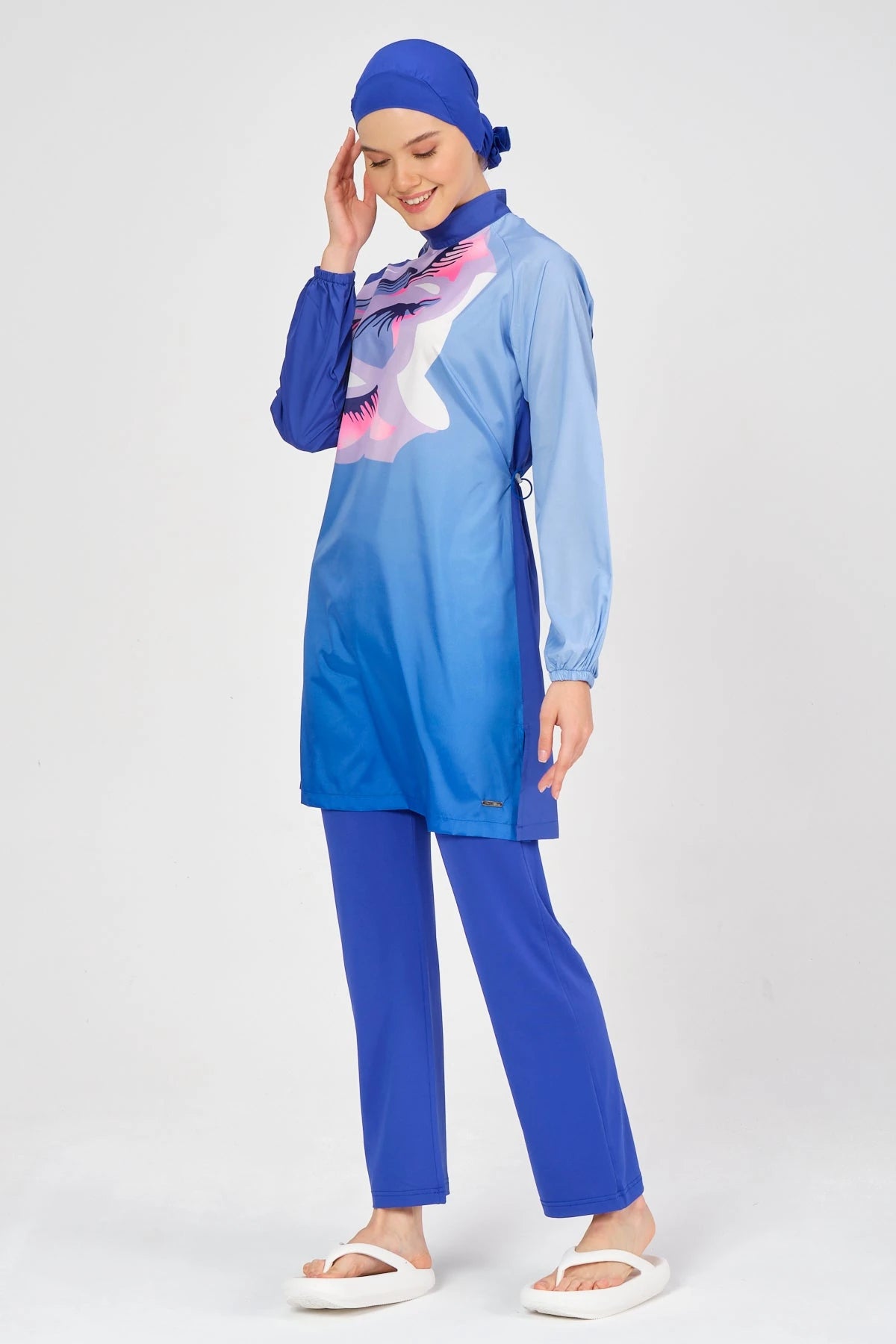 Model smiling in blue modest swimsuit with abstract print, front pose.