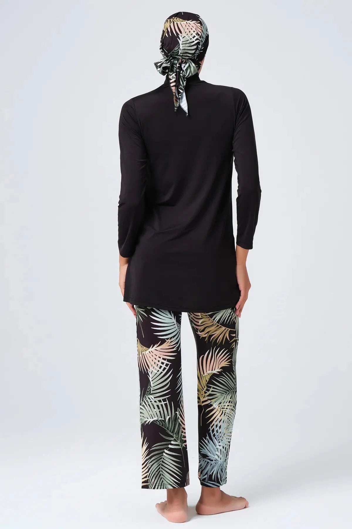 Back view of woman in black long-sleeve tunic and tropical print leggings with hijab.
