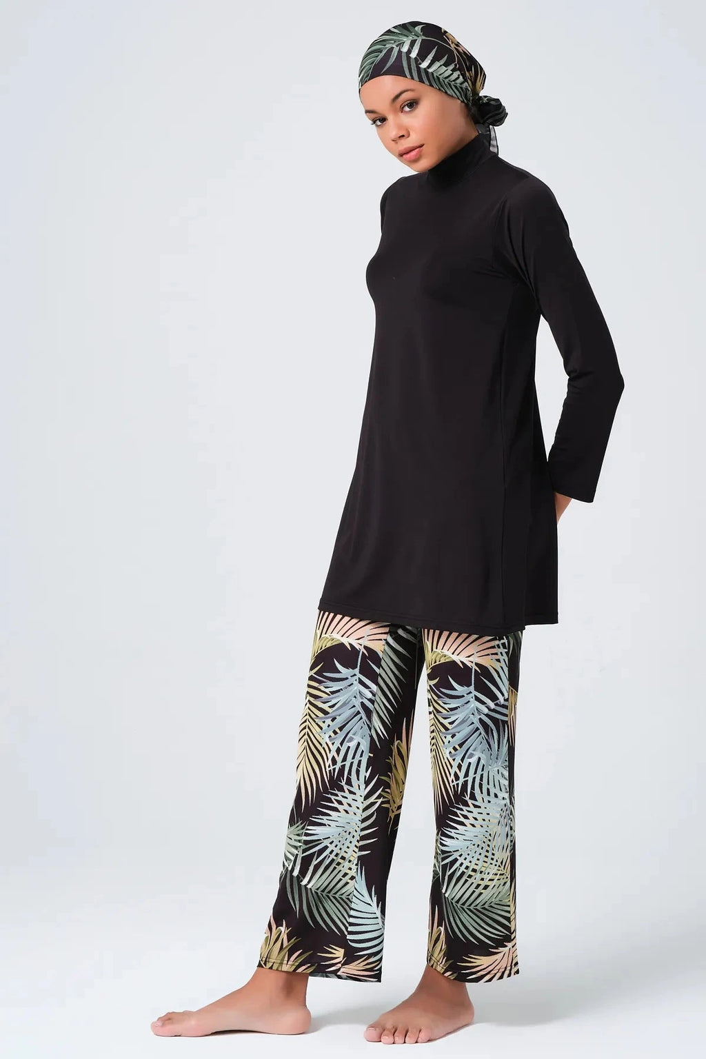 Woman in black tunic and tropical print leggings, side profile, wearing hijab.