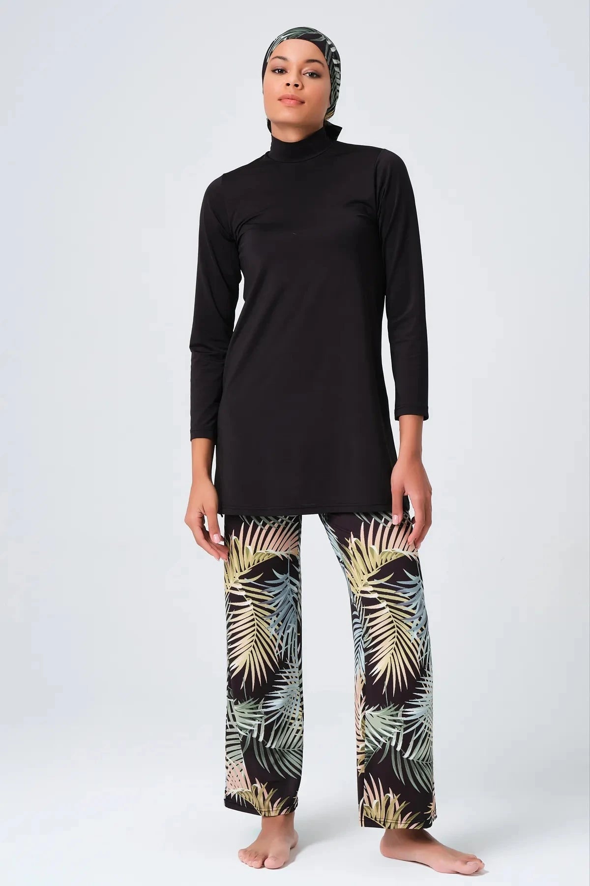 Front view of woman in black modest swimwear with tropical print leggings and hijab.