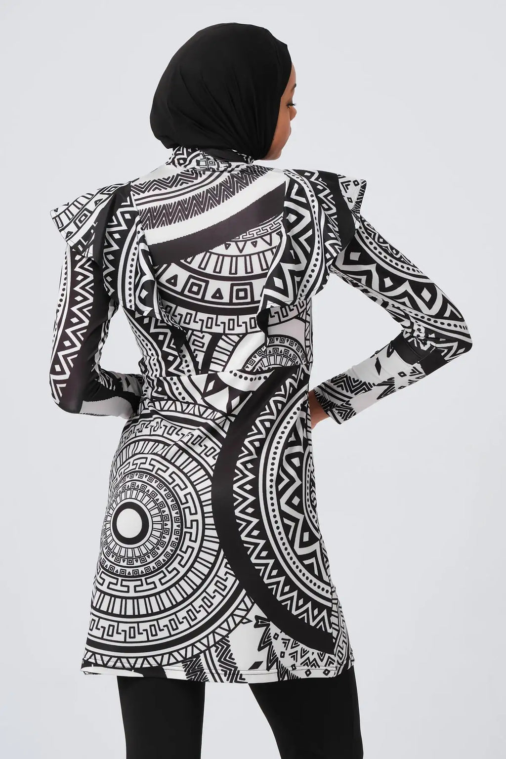 Woman in black and white tribal print burkini, back view with hands on hips.