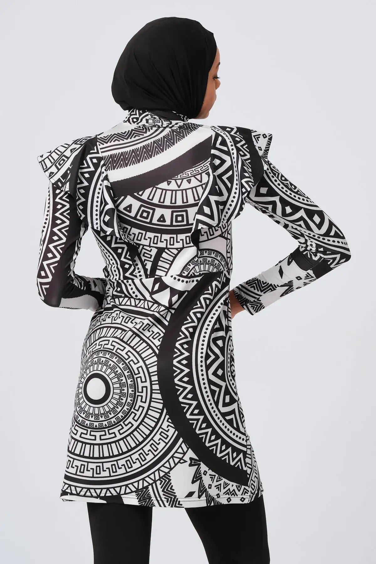 Woman in black and white tribal print burkini, back view with hands on hips.