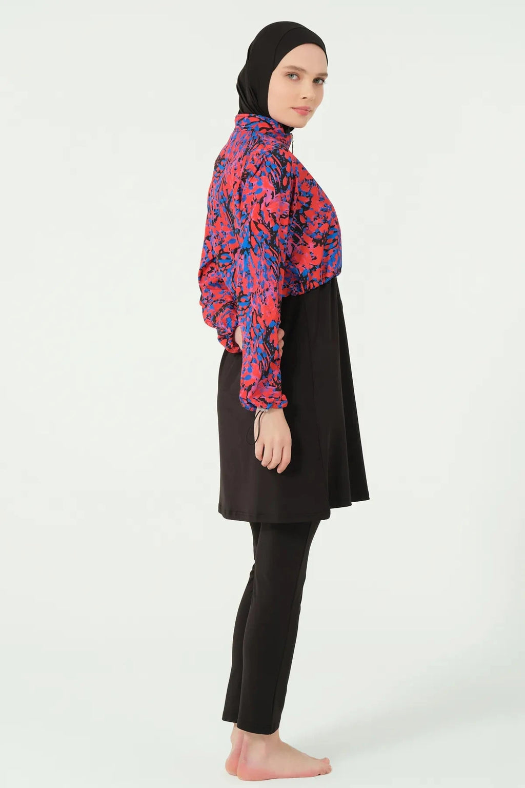 Woman in black hijab swimwear with abstract print jacket, side view.