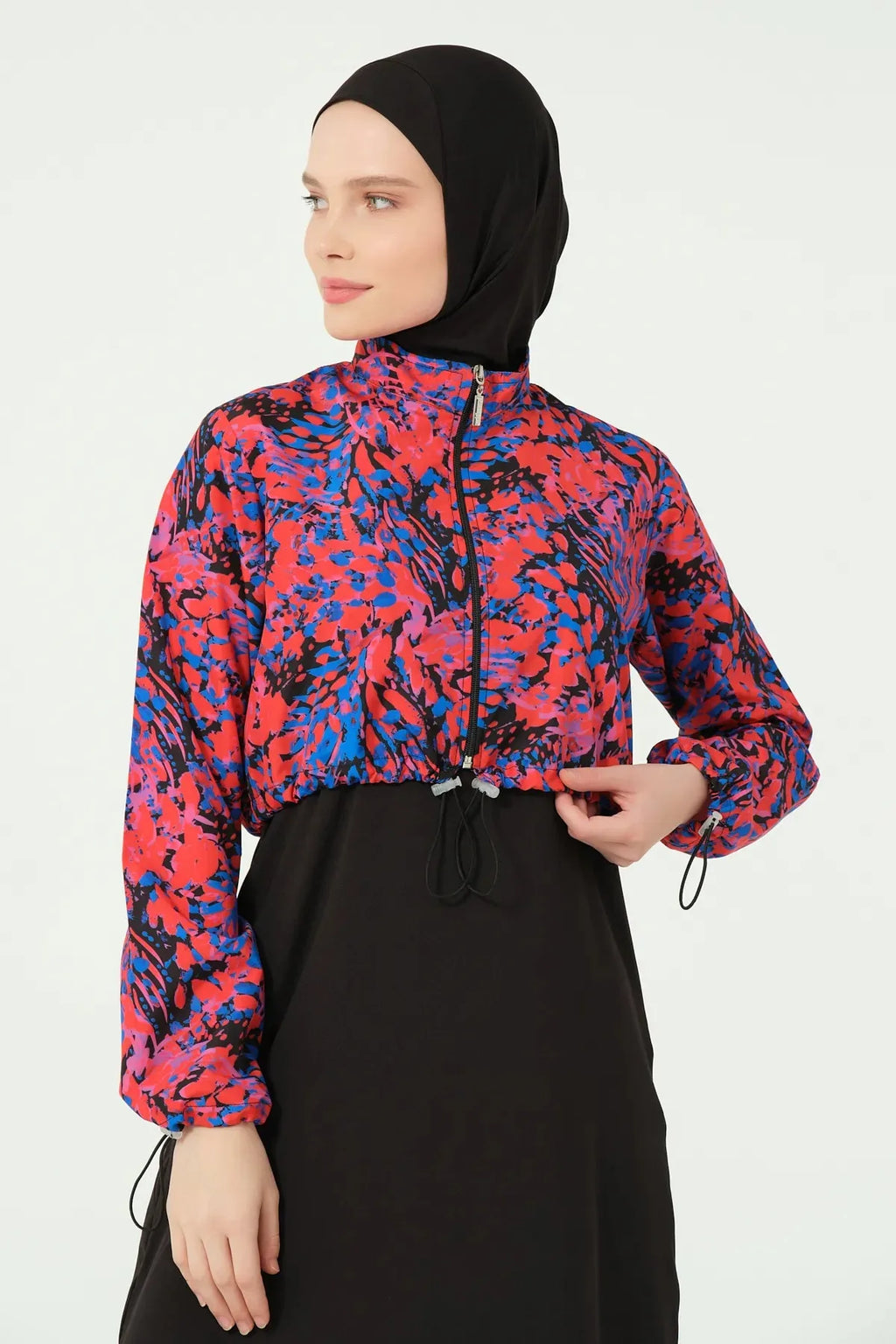 Woman adjusting drawstring on abstract print crop jacket of hijab swimwear.