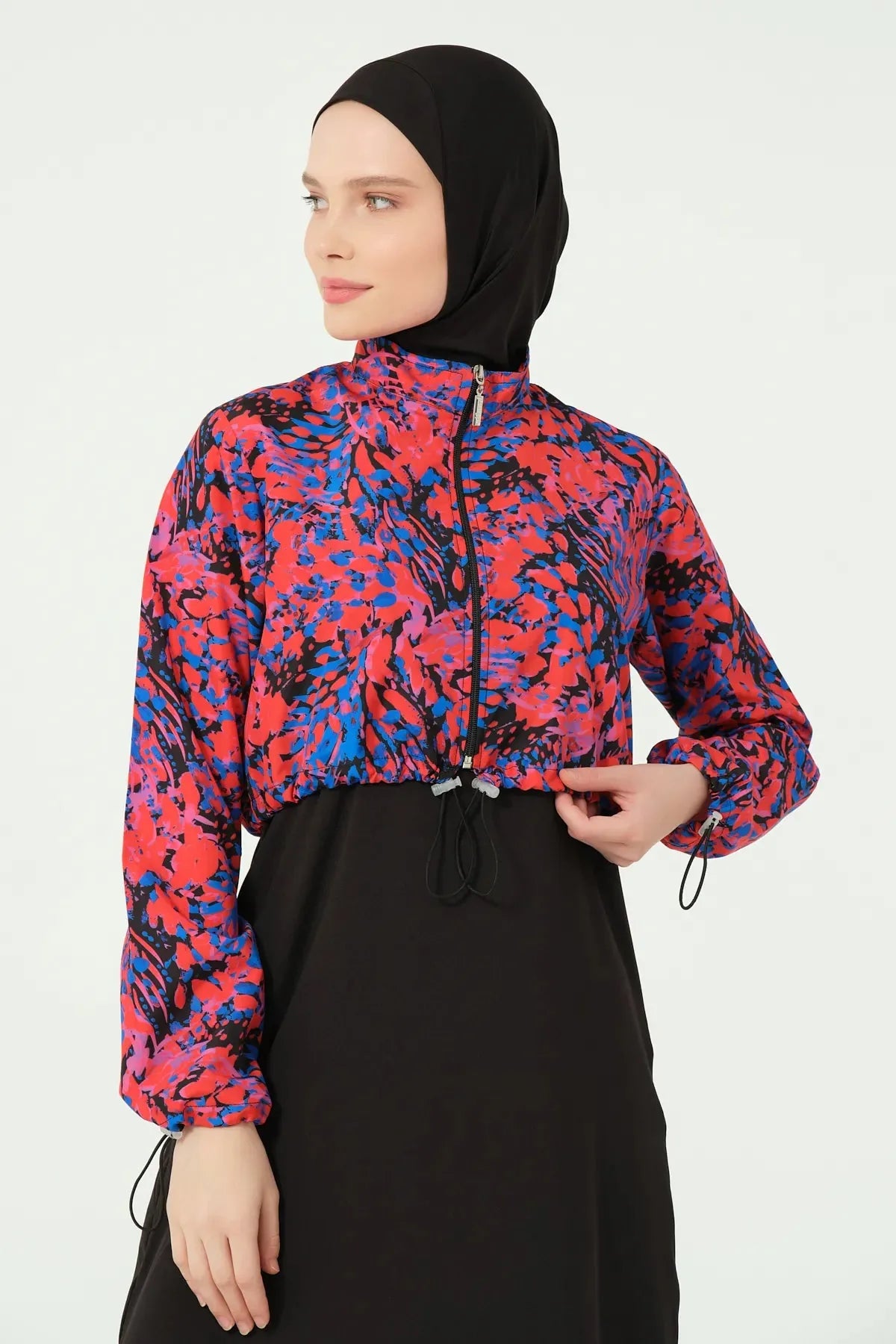 Woman adjusting drawstring on abstract print crop jacket of hijab swimwear.
