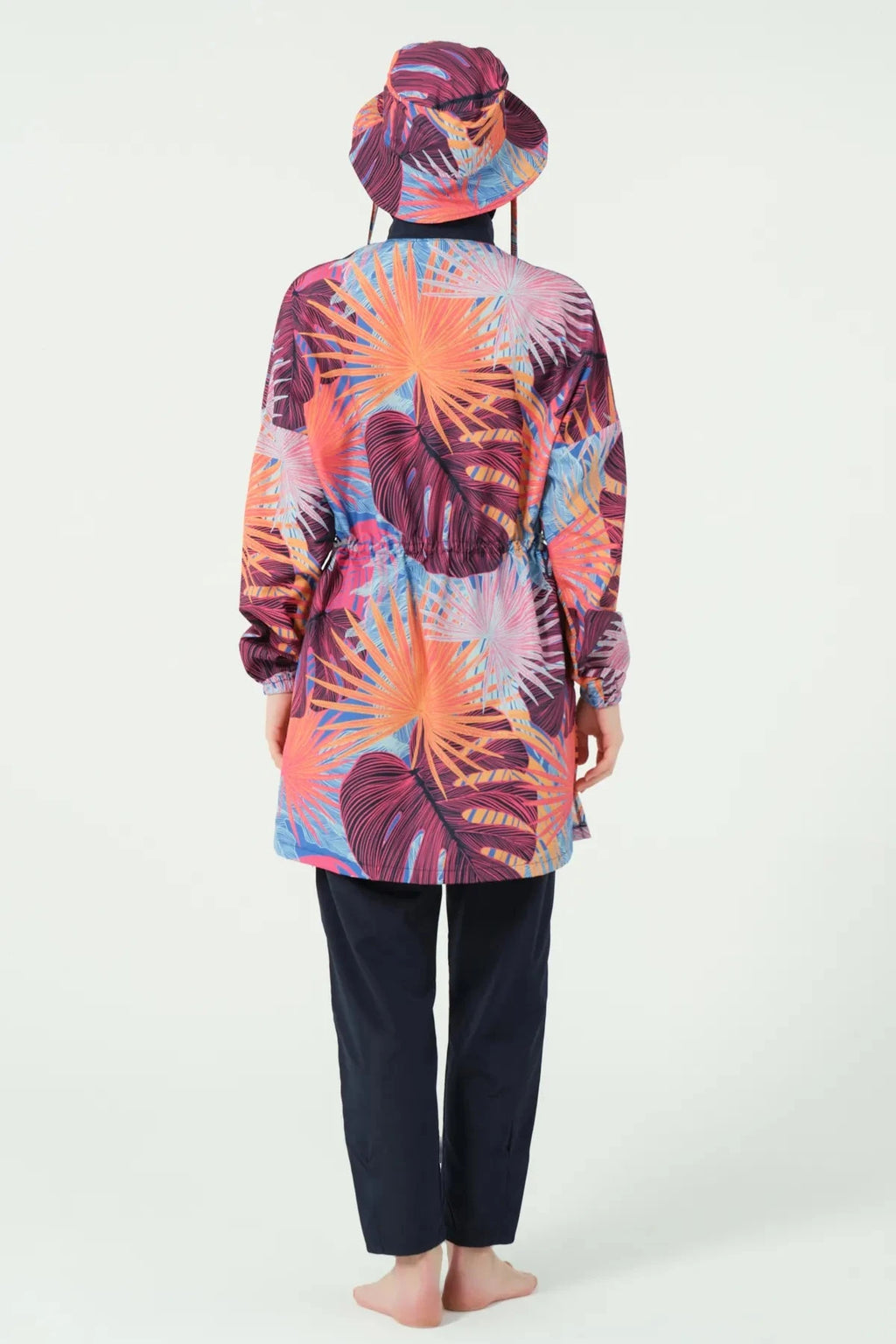Woman in tropical print modest swimwear and bucket hat, back view.