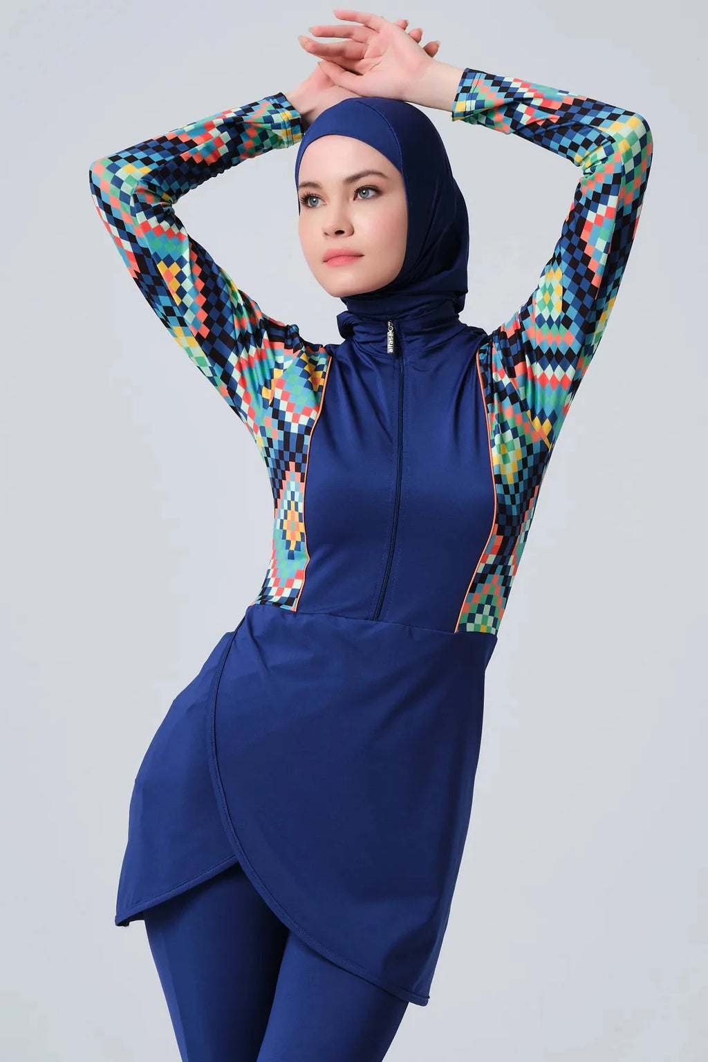Model in blue mosaic sporty burkini with arms raised on light grey background