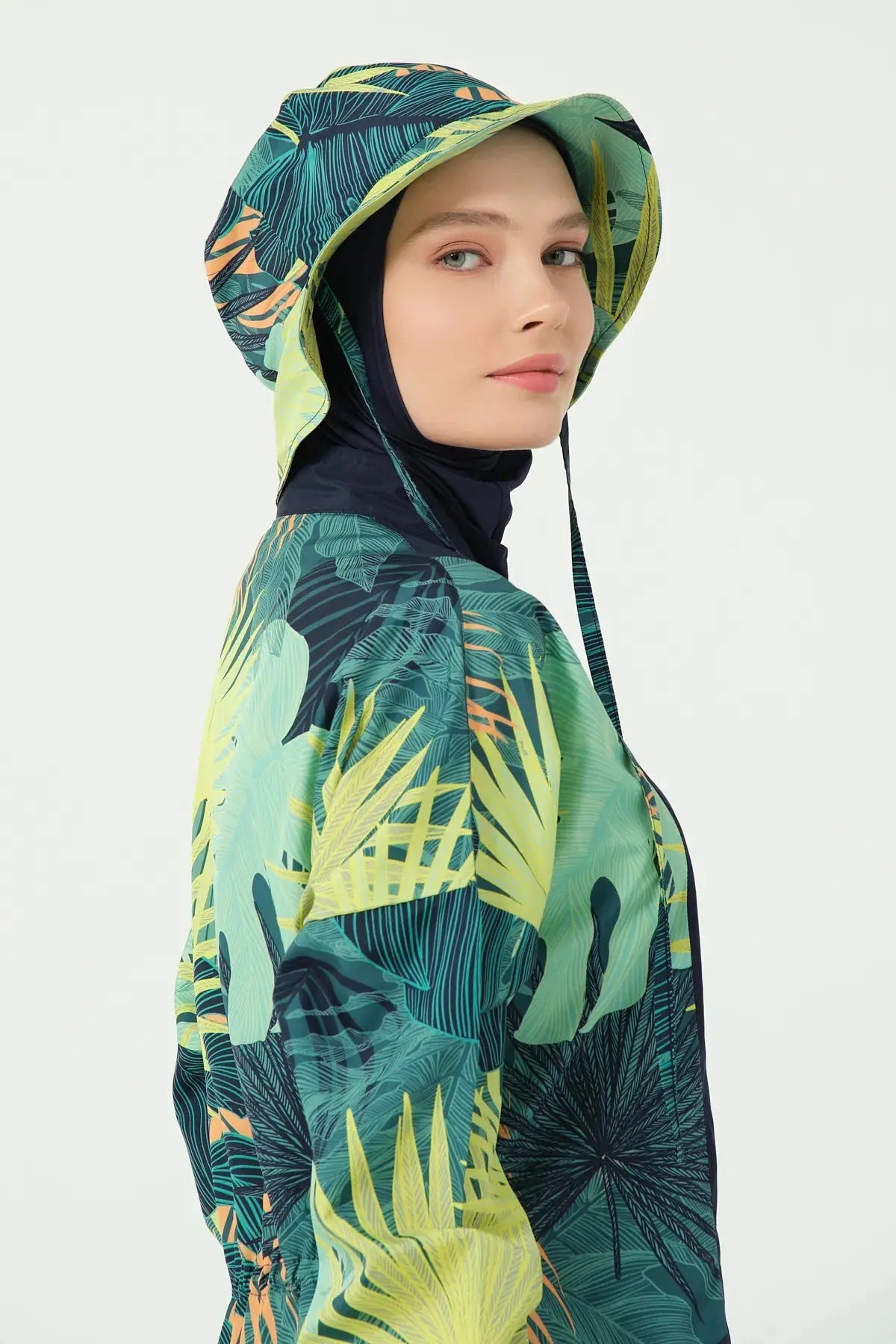 Model wearing tropical green bucket hat over navy hijab, side view.