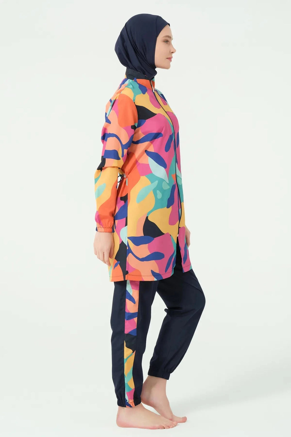 Woman in vibrant abstract print burkini set standing side profile.