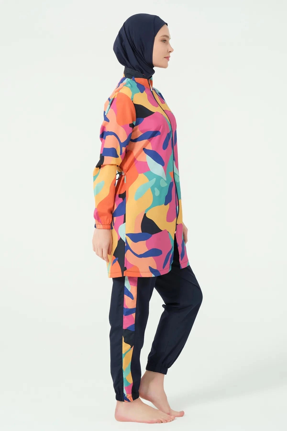 Woman in vibrant abstract print burkini set standing side profile.