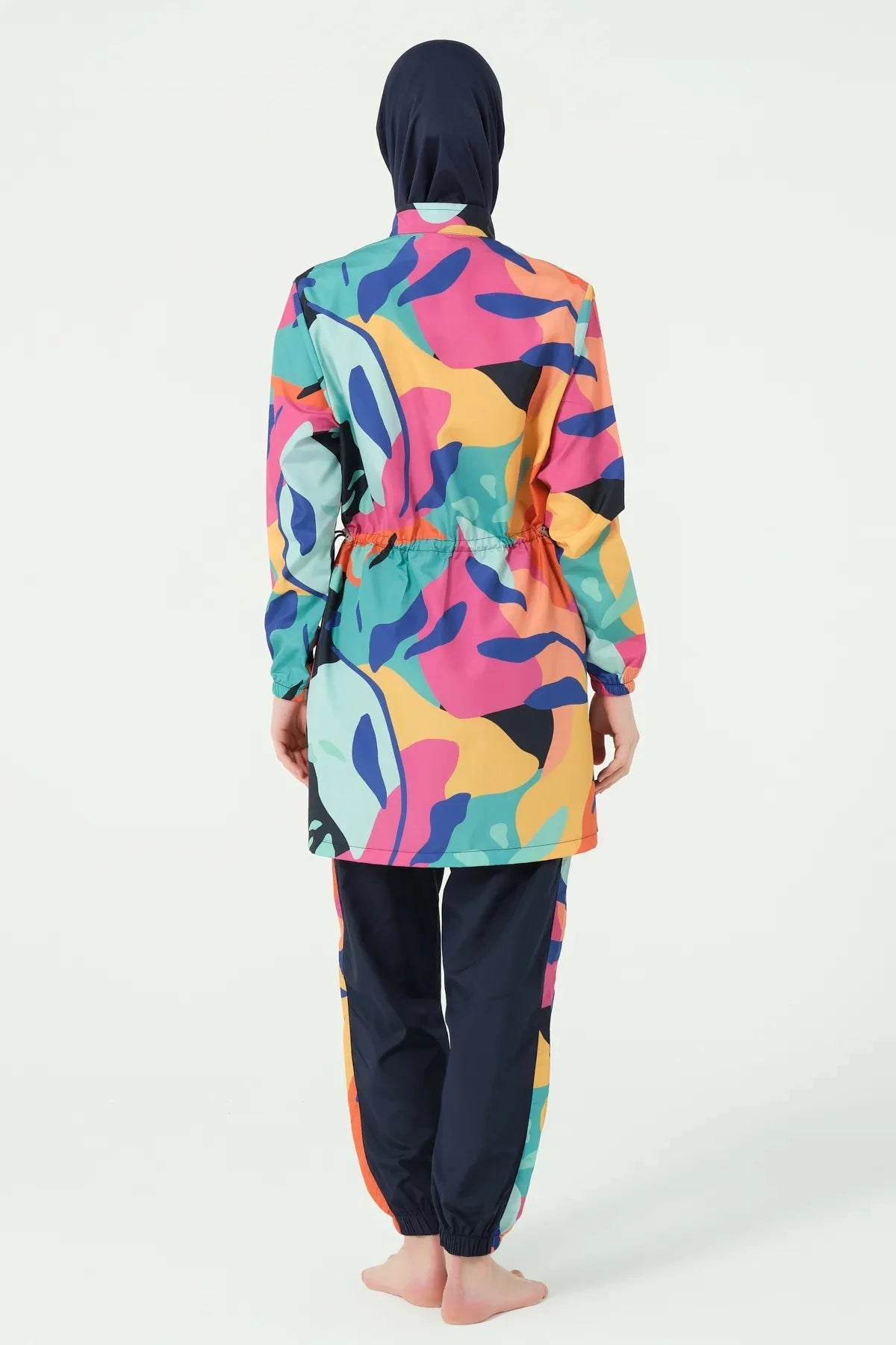 Woman in vibrant abstract print burkini set standing back view.