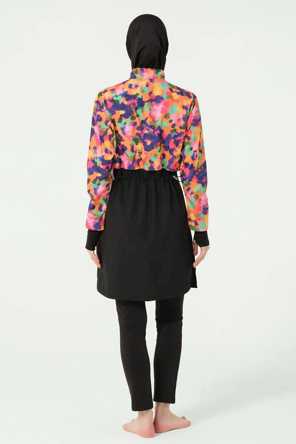 Woman in black hijab and vibrant watercolor print burkini top, back view.