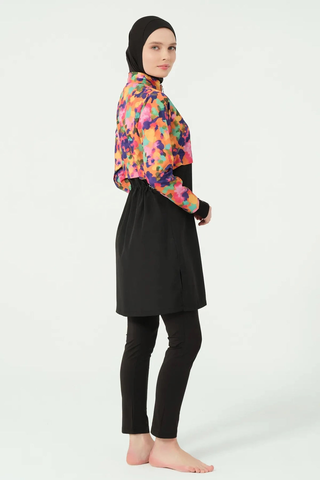 Woman in black hijab and colorful burkini set, side profile.
