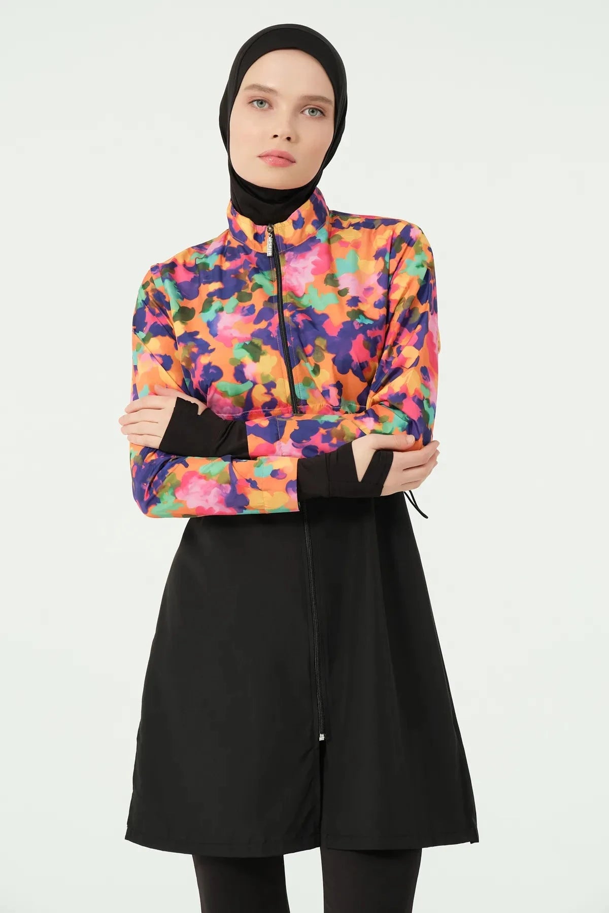 Woman in black hijab and colorful burkini set, arms crossed.