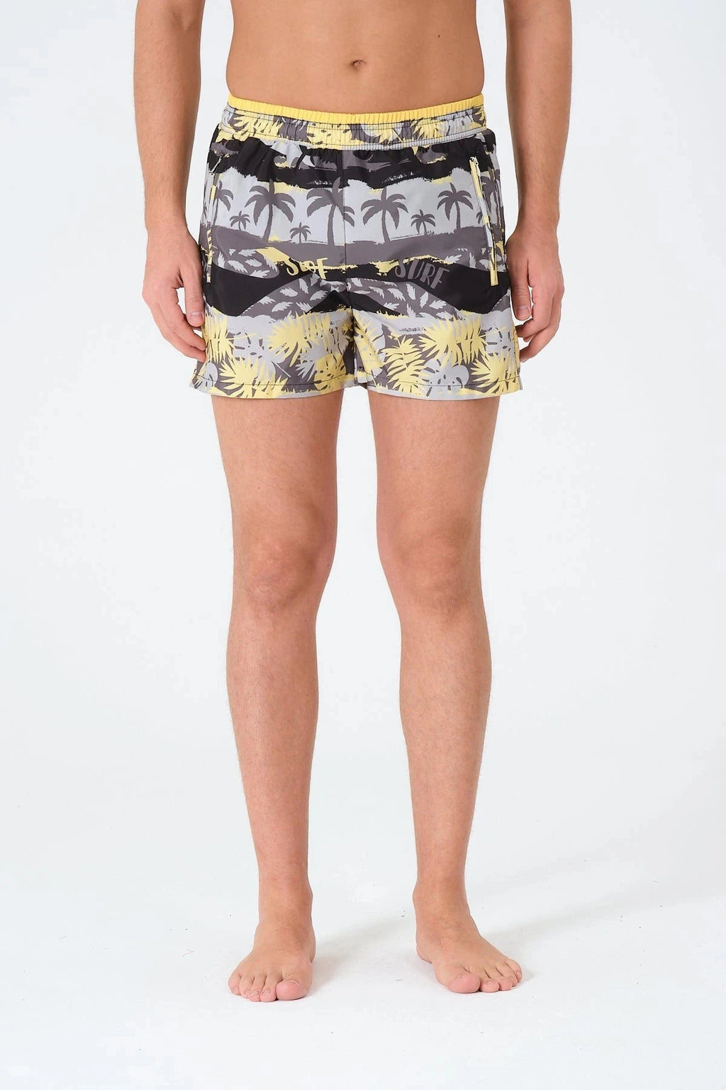 Man wearing tropical print swim trunks with yellow waistband, front view.