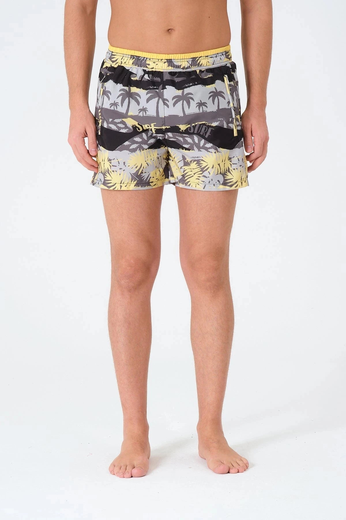 Man wearing tropical print swim trunks with yellow waistband, front view.