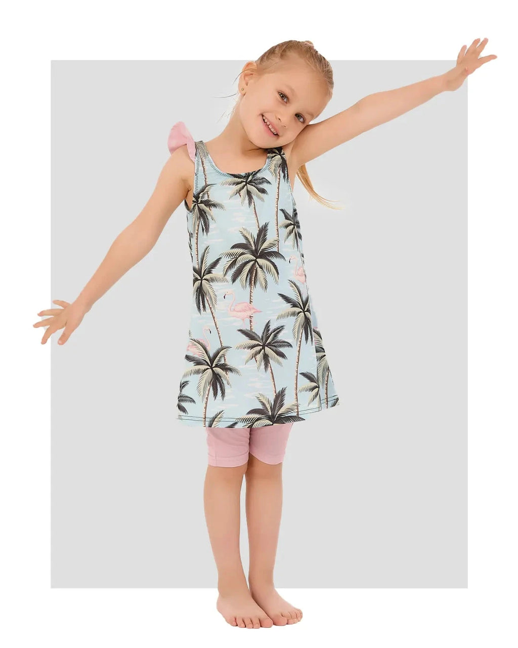 Young girl in a light blue flamingo and palm tree print modest swim dress with pink accents.