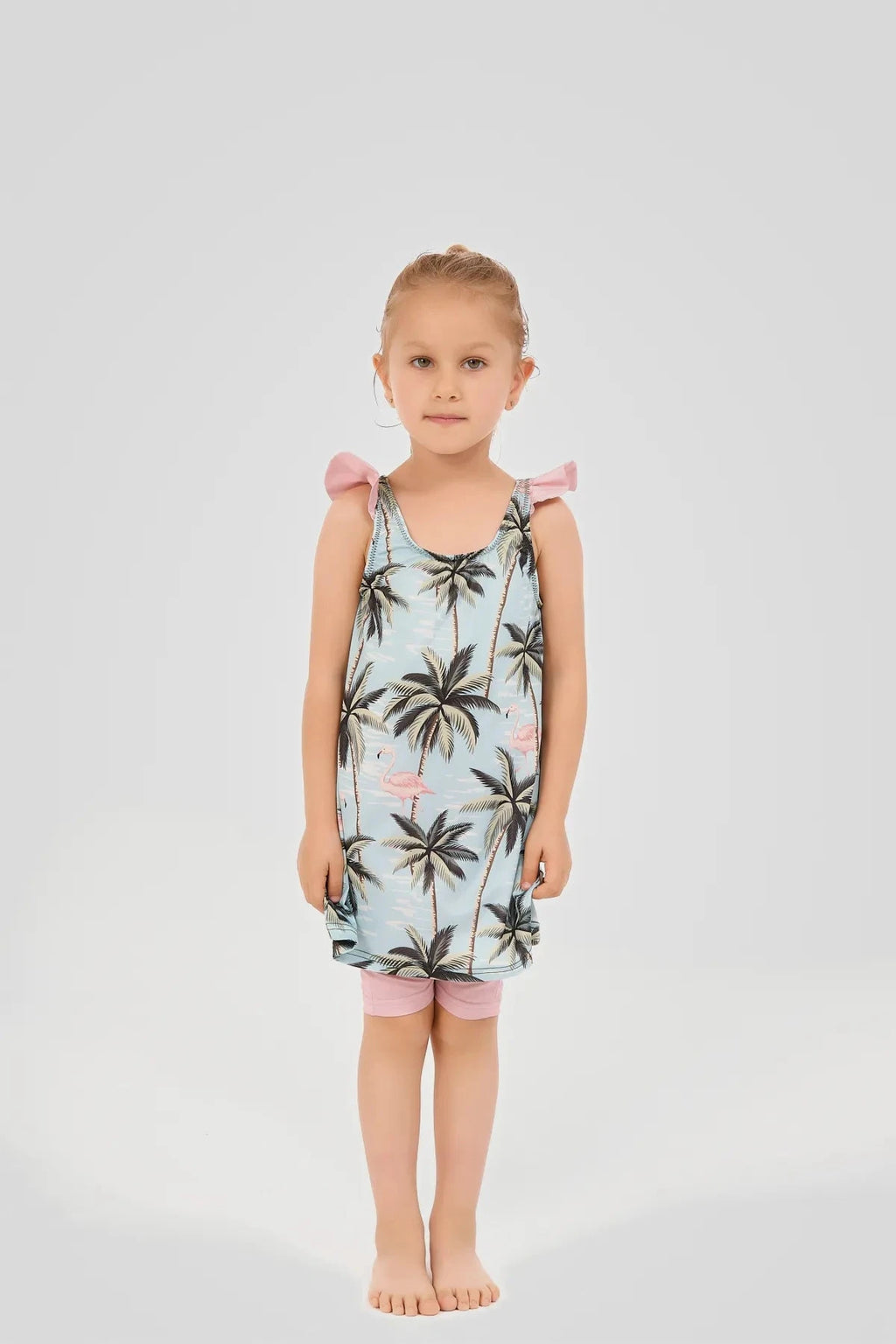 Young girl wearing a light blue flamingo and palm tree print modest swim dress, smiling.