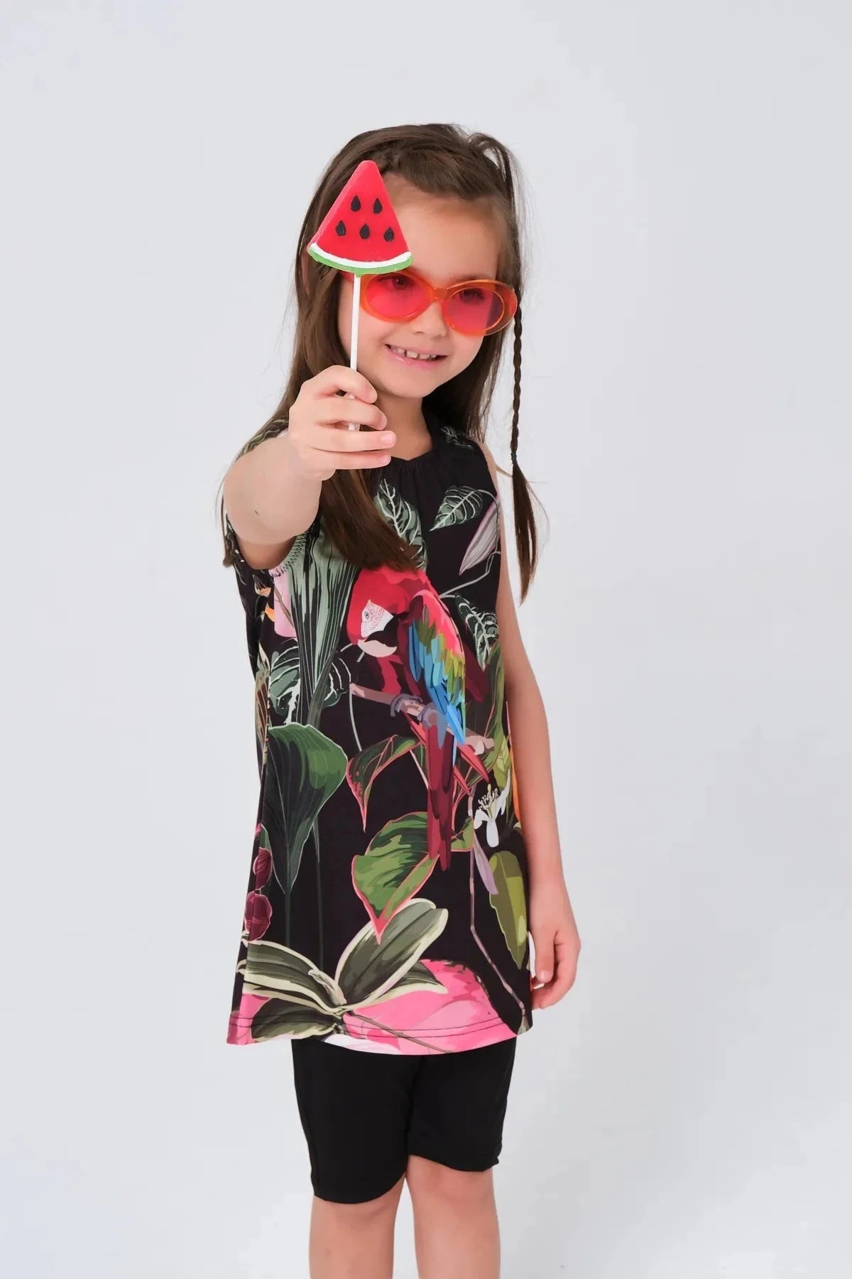 Close-up of a girl in a floral parrot print swim dress and black shorts, wearing sunglasses.