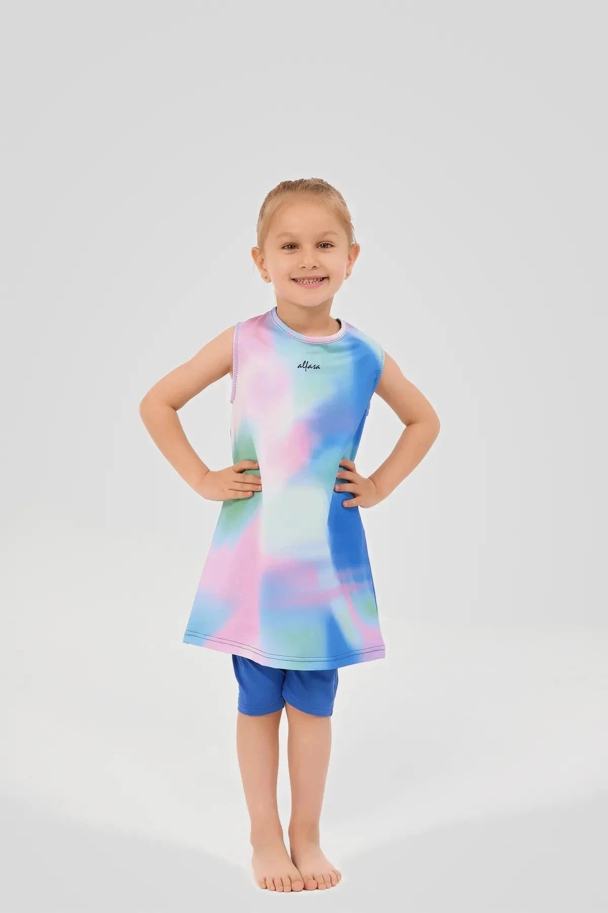 Young girl in a colorful tie-dye swim dress and blue leggings, hands on hips.