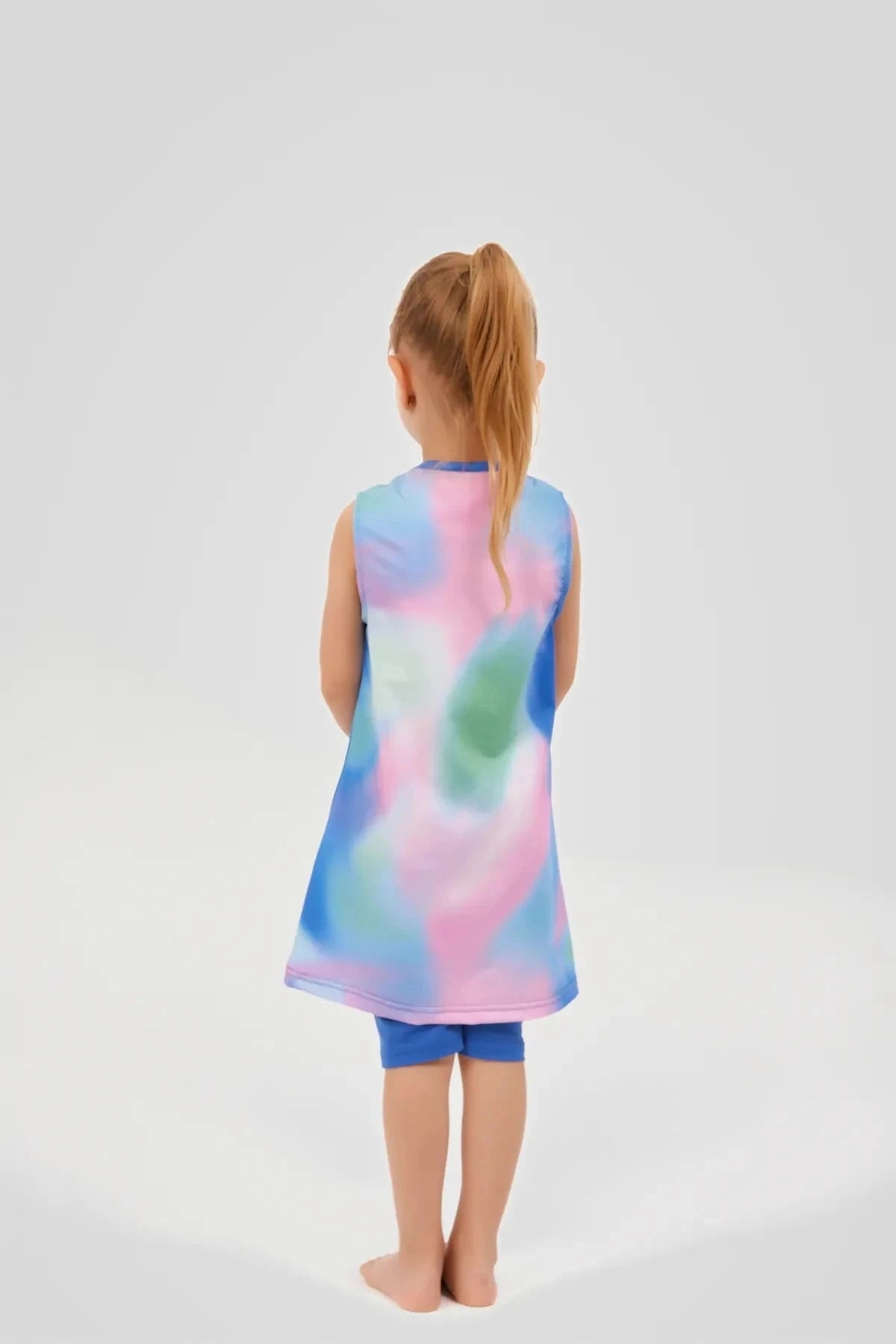 Back view of a young girl in a colorful tie-dye swim dress and blue leggings.