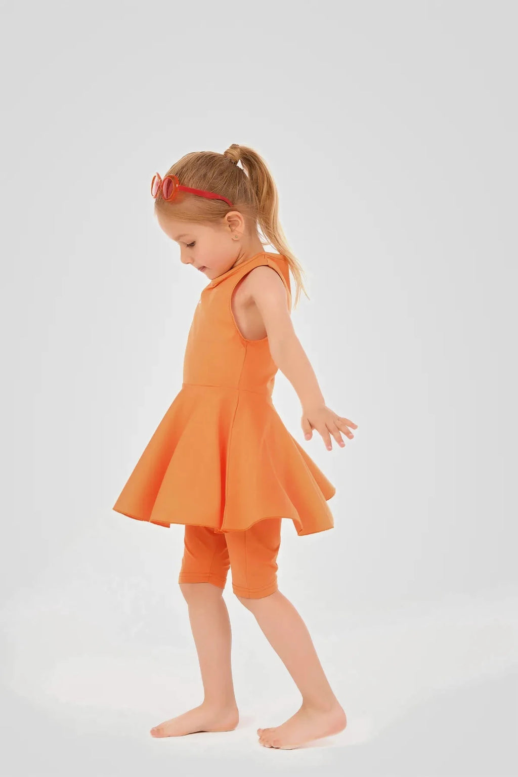 Young girl in orange modest swim dress and leggings, side view.