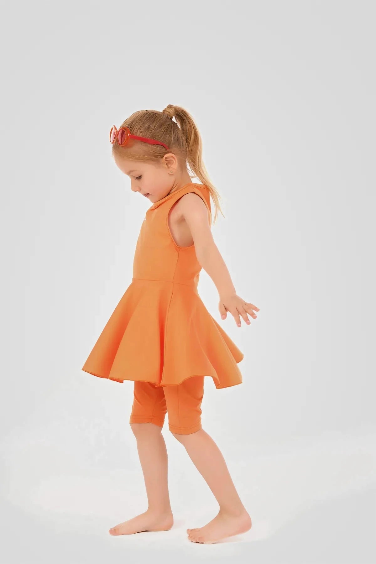 Young girl in orange modest swim dress and leggings, side view.