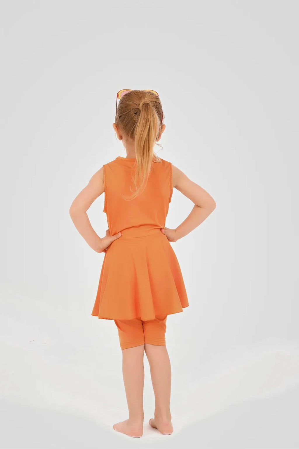 Young girl in orange modest swim dress and leggings, back view.