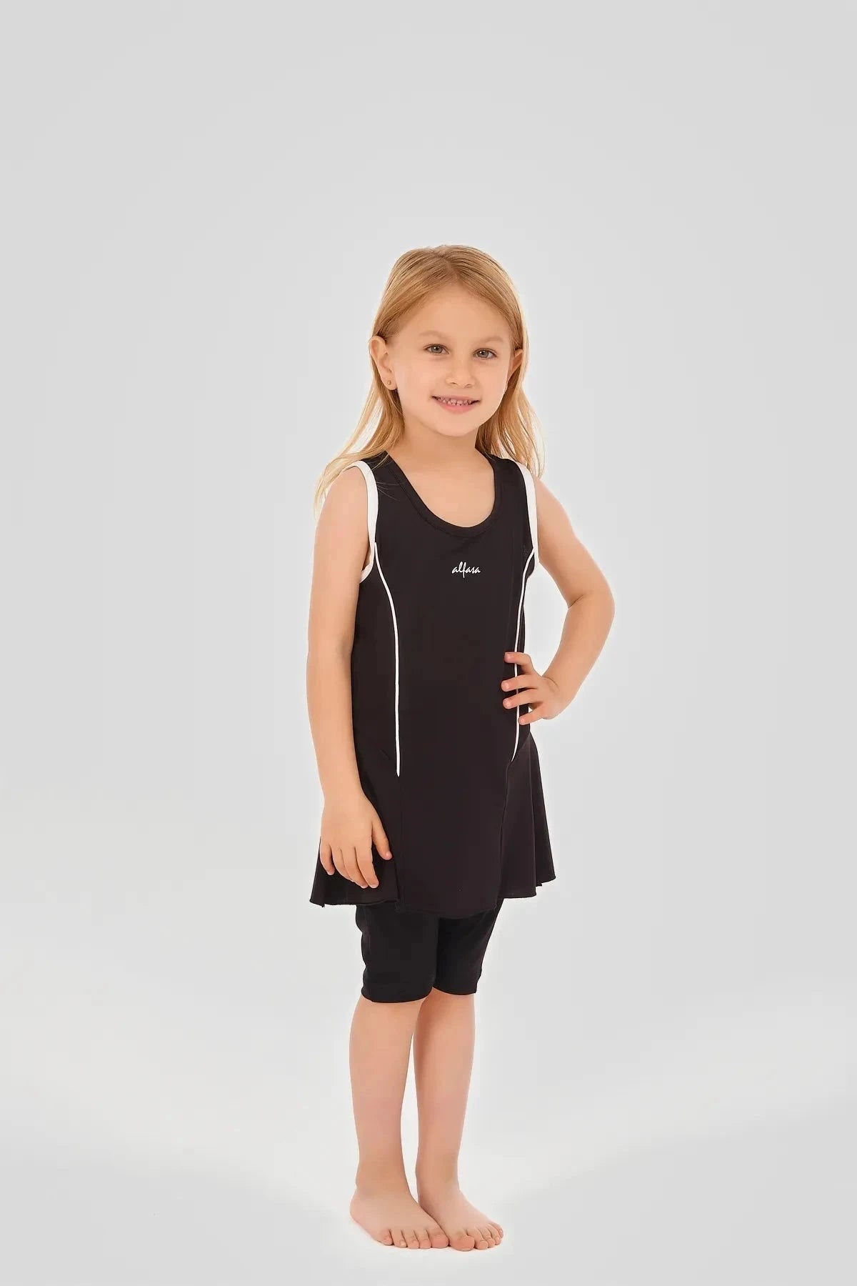 Young girl in black modest swim dress with white piping and black shorts.